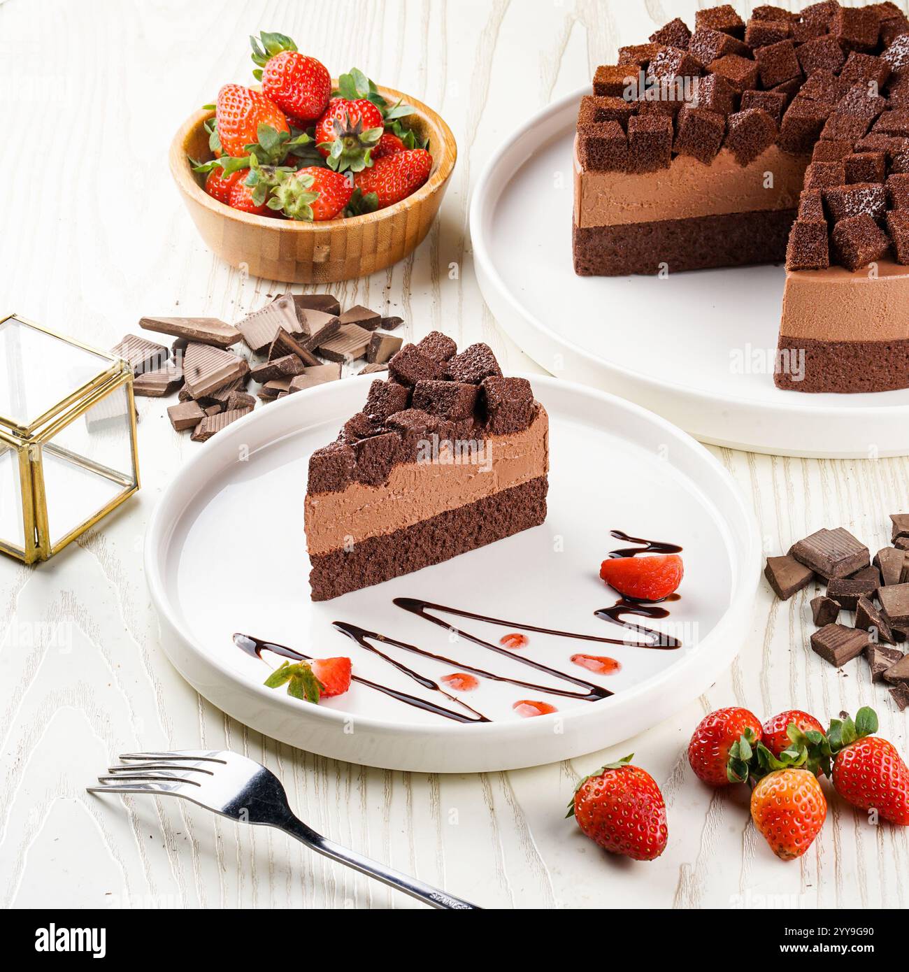 Ein wunderschön überzogenes Stück Schokoladen-Mousse-Kuchen, garniert mit Schokoladenwürfeln, garniert mit frischen Erdbeeren und Schokoladennebel Stockfoto