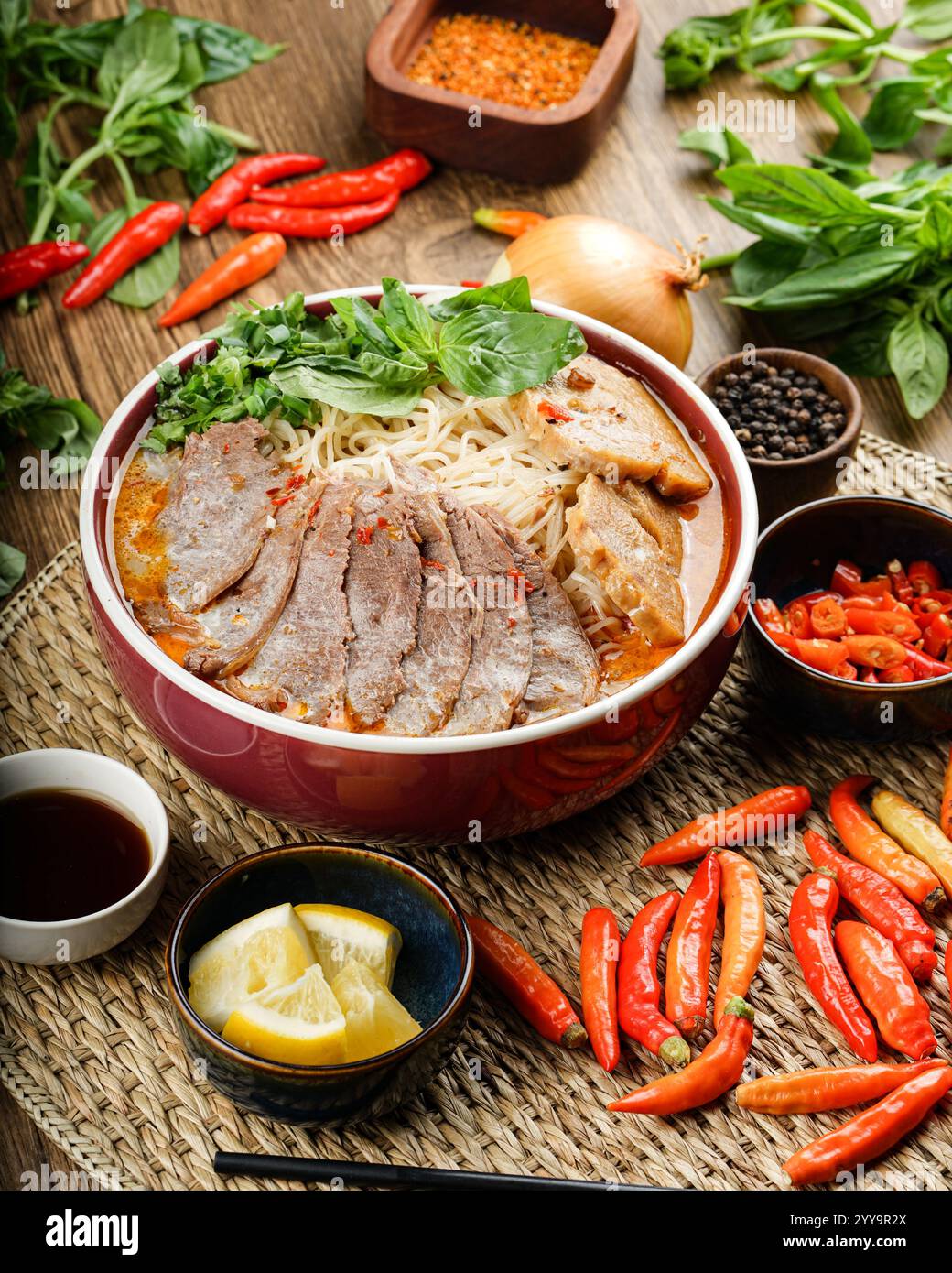 Eine vibrierende Schüssel mit scharfer vietnamesischer Rindfleischnudelsuppe (bún Bò Huế), die mit frischen Kräutern, Chili und zarten Rindfleischscheiben gefüllt ist, ein authentischer Geschmack von Vietnam Stockfoto