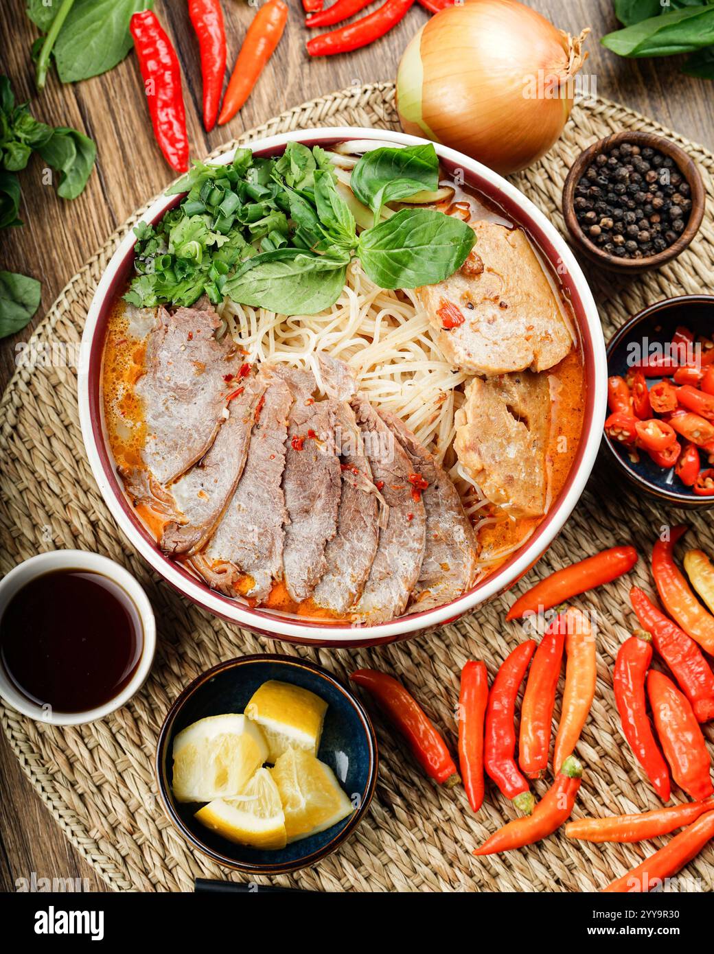 Eine vibrierende Schüssel mit scharfer vietnamesischer Rindfleischnudelsuppe (bún Bò Huế), die mit frischen Kräutern, Chili und zarten Rindfleischscheiben gefüllt ist, ein authentischer Geschmack von Vietnam Stockfoto