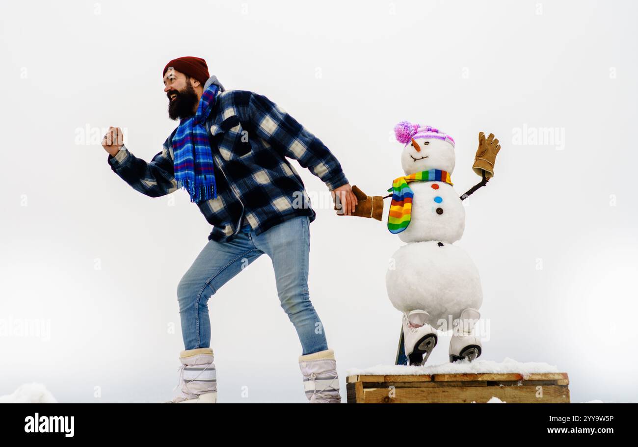 Weihnachten und Neujahrsfeier. Glücklicher bärtiger Mann im karierten Mantel mit Schneemann auf Schlittschuhen. Aktive Freizeit, Wintersport. Mann in Winterkleidung ru Stockfoto