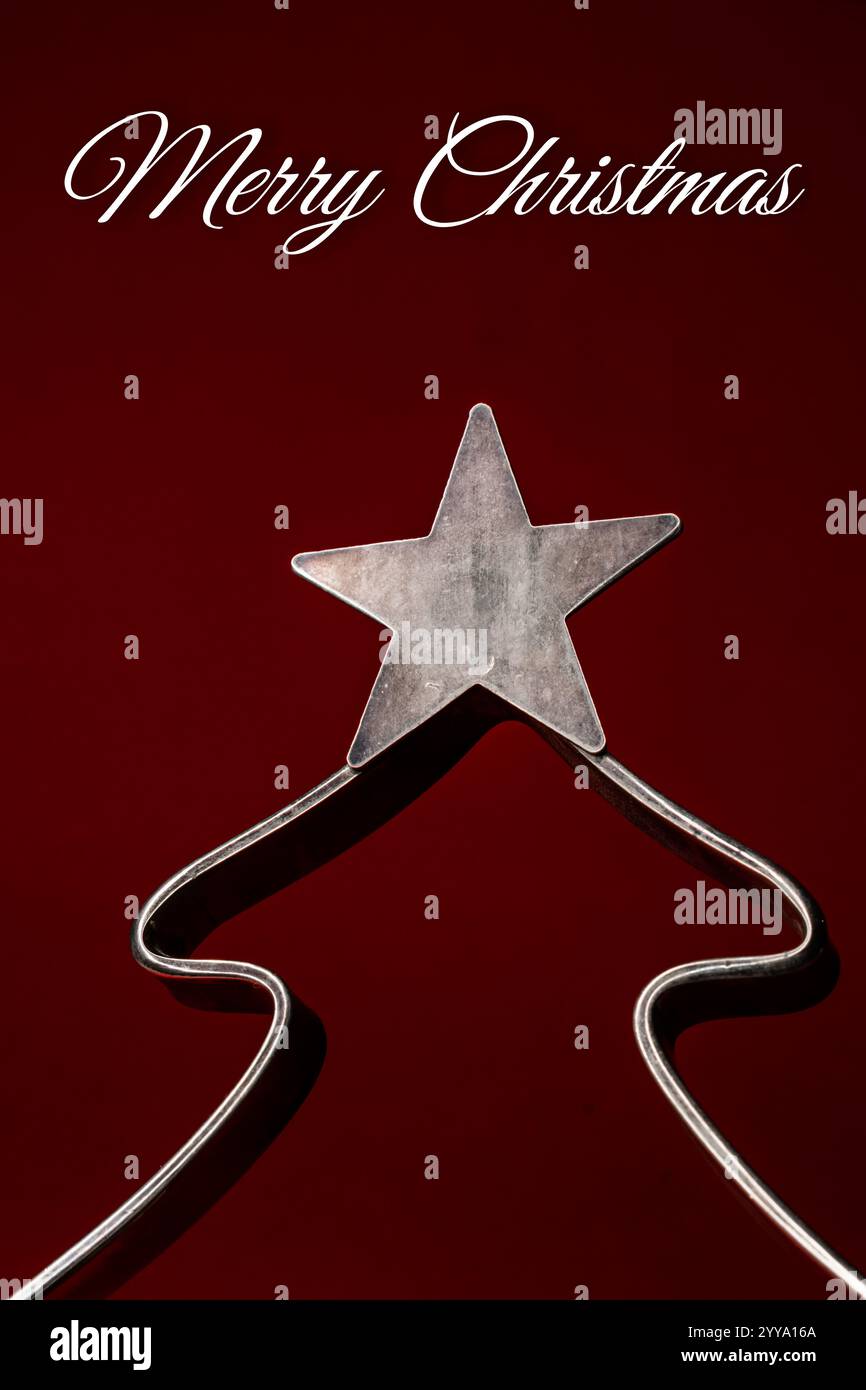 Metall-weihnachtsbaumdekoration mit Stern auf einem burgunderroten Hintergrund mit MERRY CHRISTMAS Text Stockfoto