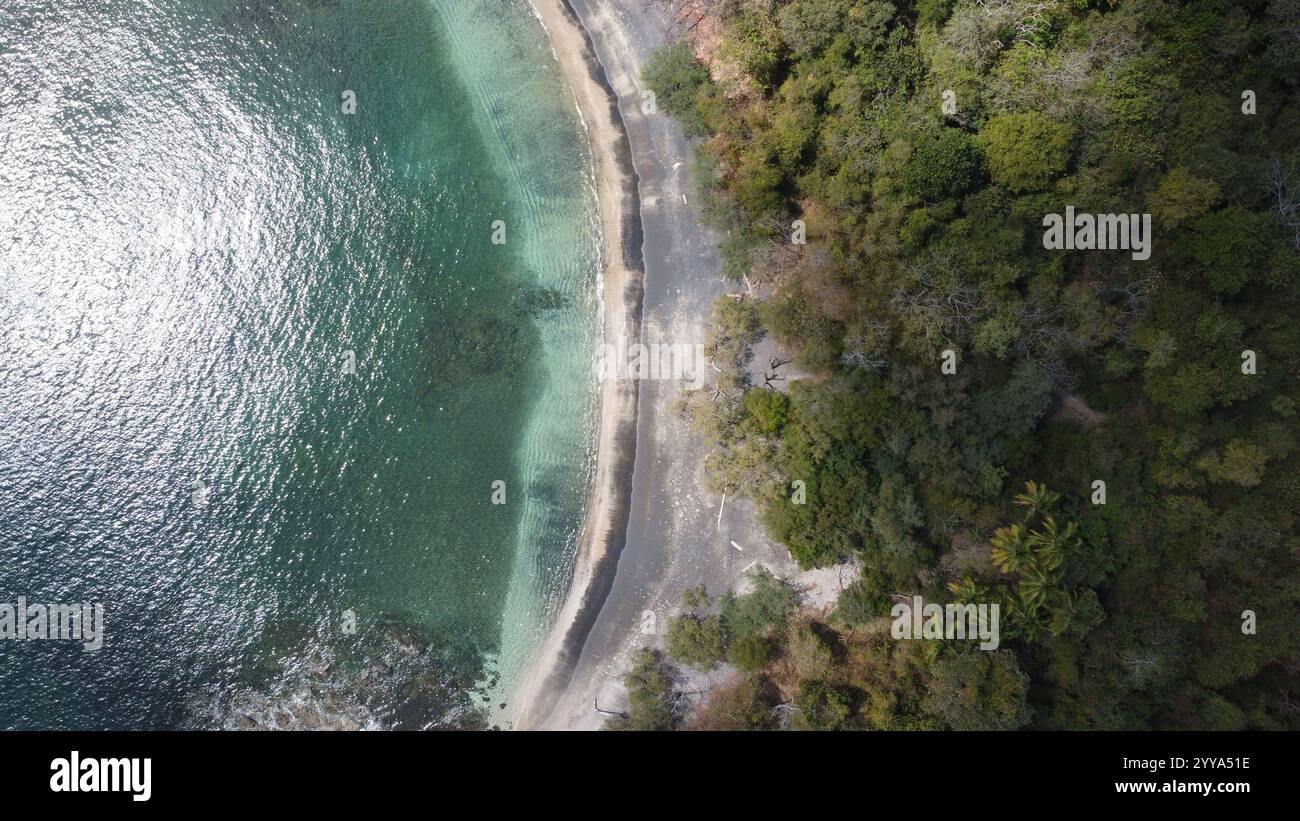 Blick von der Drohne auf eine abgelegene tropische Bucht mit kristallklarem türkisfarbenem Wasser, umgeben von üppig grünen Wäldern und felsiger Küste Stockfoto