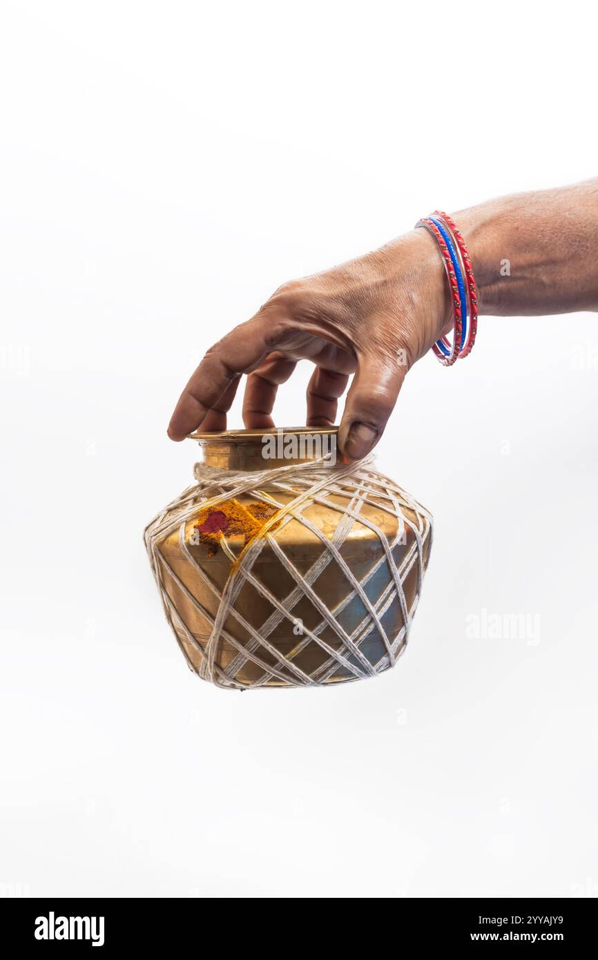 Nahaufnahme einer Hand, die ein Messingglas hält, das mit Streicher und traditionellen Dekorationen auf weißem Hintergrund verziert ist. Geeignet für Tradition, Rituale, ethnische Stockfoto