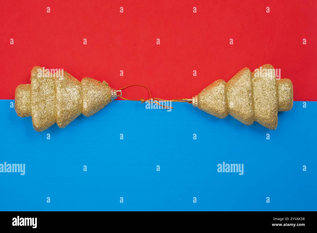 Elegante goldene Glitzer-Weihnachtsbaumdekorationen auf blauem und rotem gespaltenem Hintergrund. Perfekt für Feiertagsthemen, festliche Feiern und Stockfoto