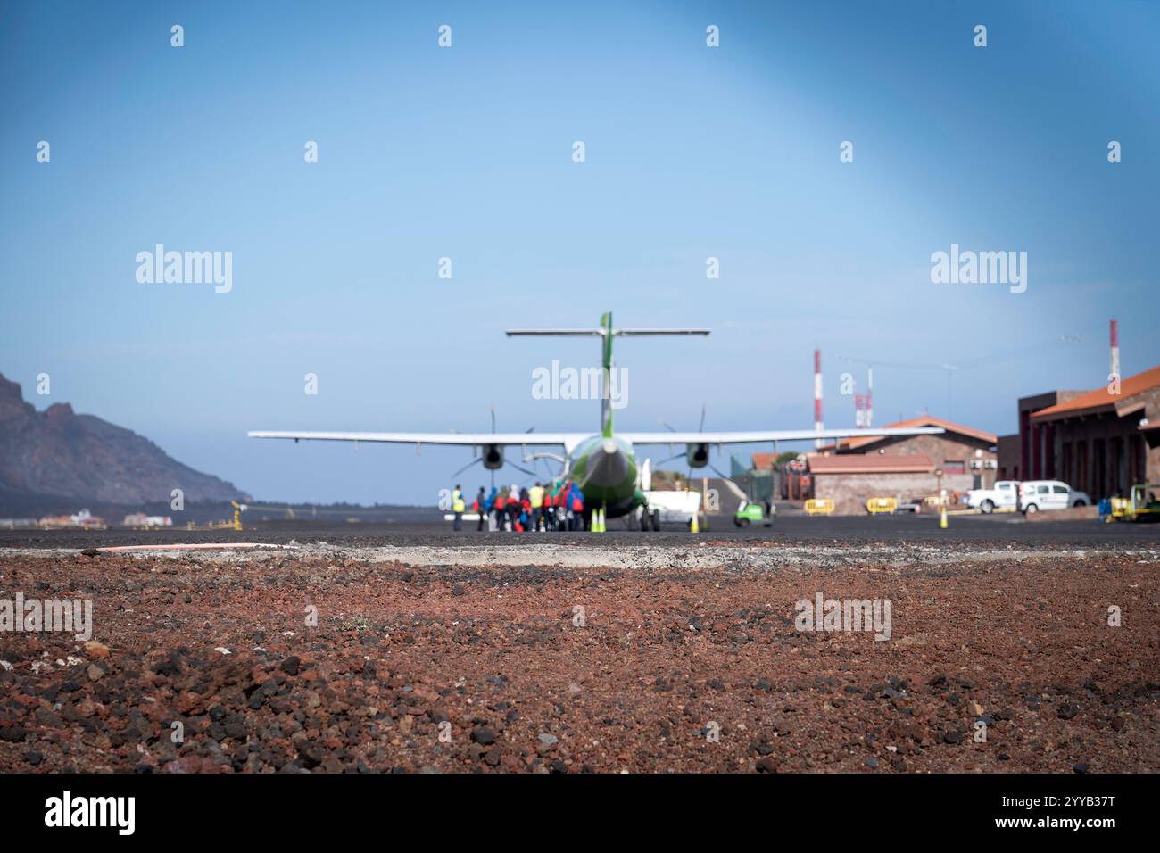 Refugees Boarding a Propeller Plane at a Remote Airport with Volcanic Landscape Stockfoto