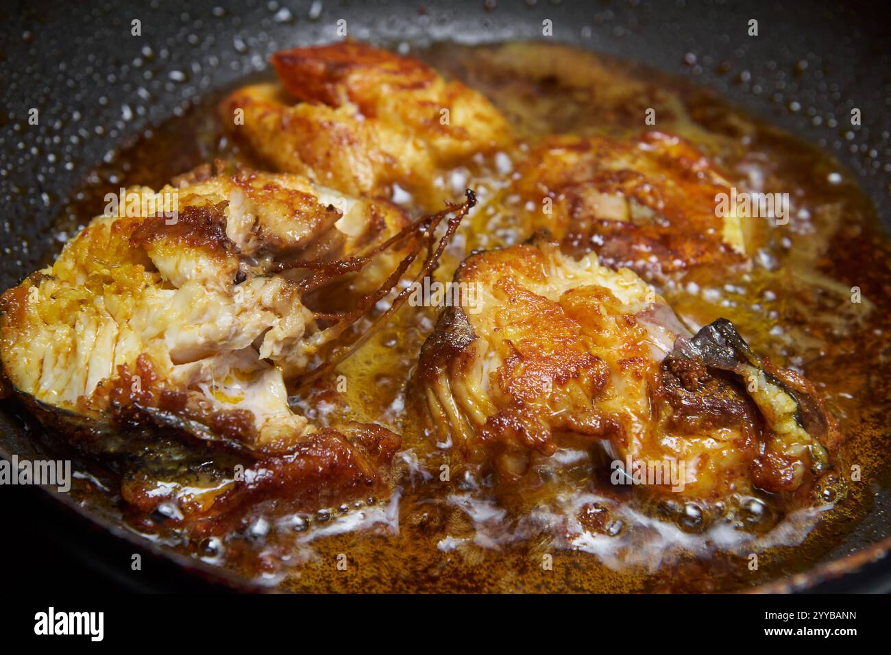 Nahaufnahme von gewürzten oder marinierten Fischstücken, die in Kokosöl gebraten werden, goldbrauner knuspriger Fisch mit sprudelndem und glitzerndem Öl, Seitenwinkel Stockfoto