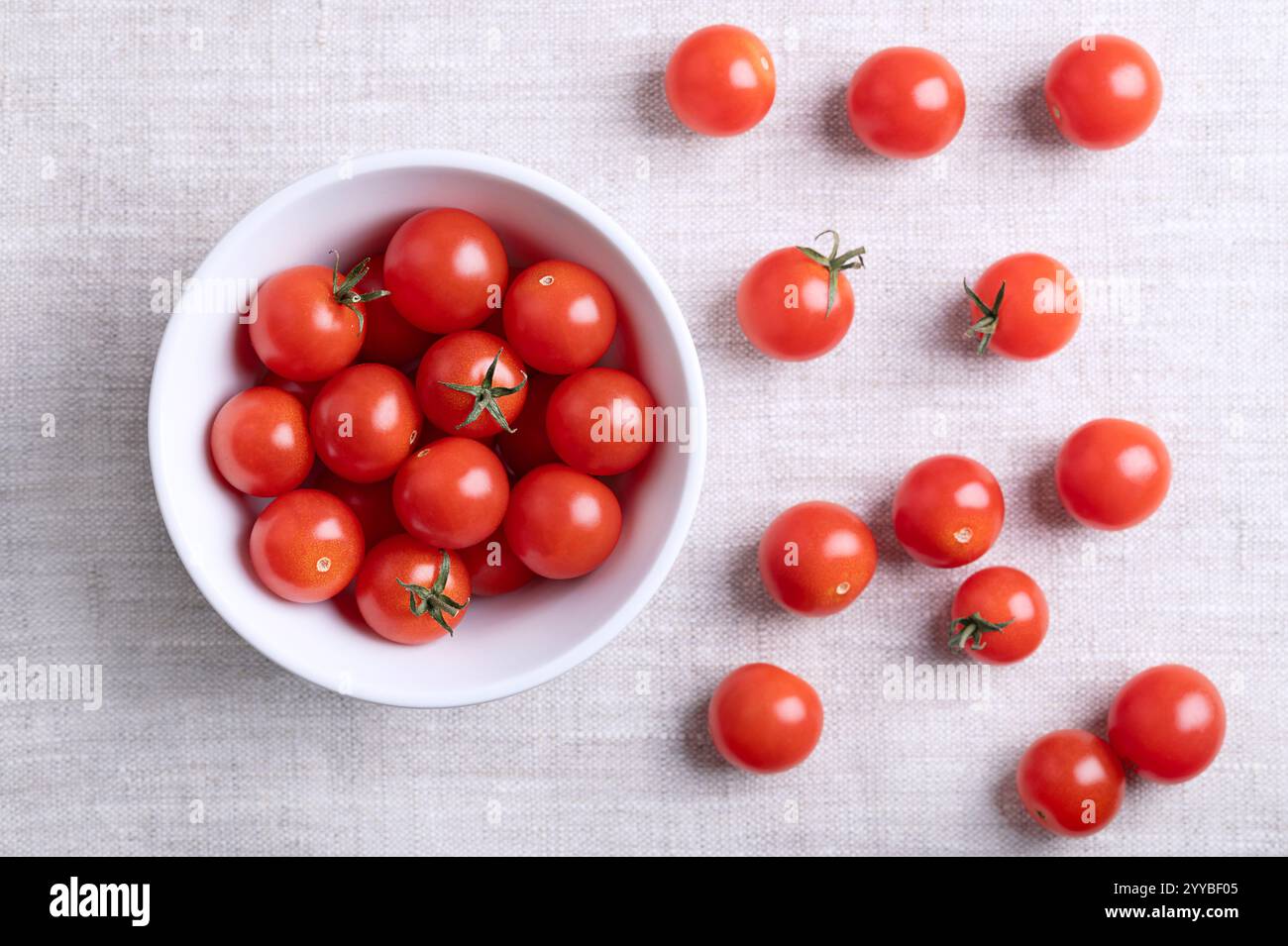 Kleine rote Kirschtomaten in einer weißen Schüssel auf Leinenstoff, von oben. Frische, reife, winzige und runde Cocktailtomaten der Art Solanum lycopersicum. Stockfoto