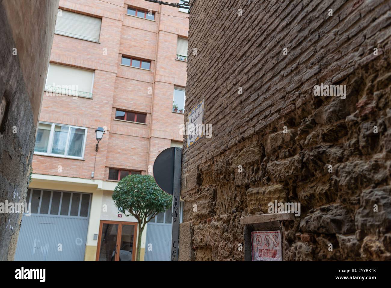 Logrono, La Rioja, Spanien. Dezember 2024. Die Straße Ochavo, die sich im Herzen der Altstadt von Logroño befindet, ist ein einzigartiges Beispiel für die mittelalterliche Struktur der Stadt. Nur wenige Meter lang, verbindet diese malerische Straße mit der Villanueva Straße und gilt als die kleinste Straße in der Hauptstadt La Rioja. Der Name leitet sich möglicherweise von einer antiken Münze, dem Ochavo, ab, und seine enge ist Zeugnis der mittelalterlichen Stadtplanung. Heute ist die Straße Teil eines Gebiets, in dem die städtische Revitalisierung vor Herausforderungen steht, in dem historische Gebäude, die einer Sanierung bedürfen, mit anderen, die eine haben, nebeneinander existieren Stockfoto