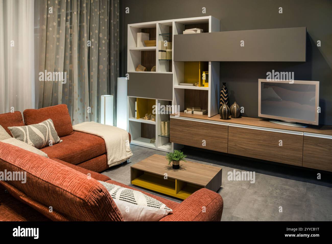 Stilvolles, modernes Wohnzimmer mit komfortablem rotem Sofa, großem fernseher und modernen Möbeln für eine gemütliche und einladende Atmosphäre Stockfoto