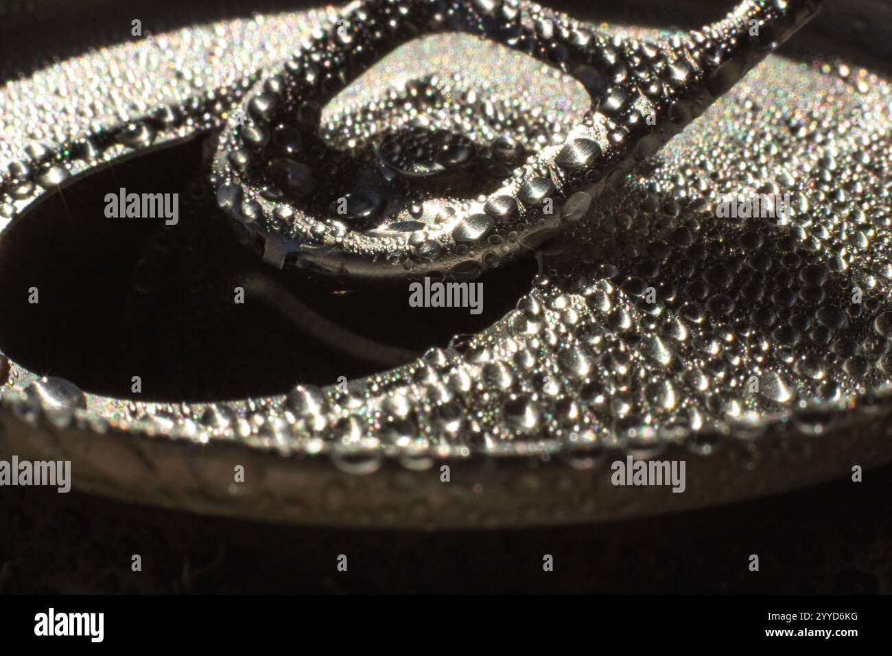 Eine Makroaufnahme der Öffnungslasche einer Aluminiumnatron-Dose, die mit Tautropfen bedeckt ist. Die Wassertropfen glitzern im Sonnenlicht und die detaillierten Texturen Stockfoto