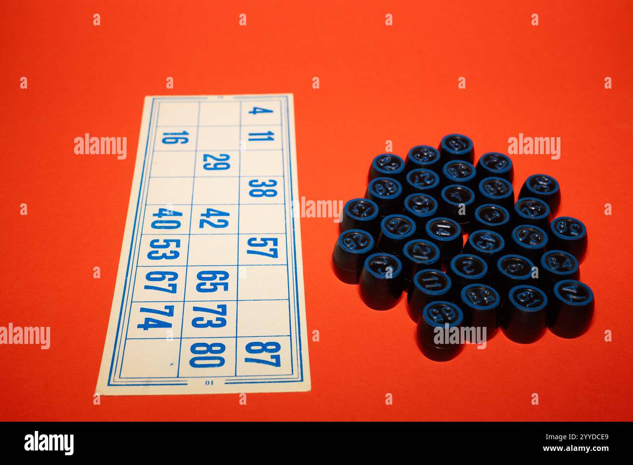 Eine Bingo-Karte befindet sich neben einer Sammlung blauer Marker auf einem leuchtenden orangefarbenen Hintergrund. Die Spielelemente sind bereit für Enthusiasten, mit dem Spiel zu beginnen Stockfoto