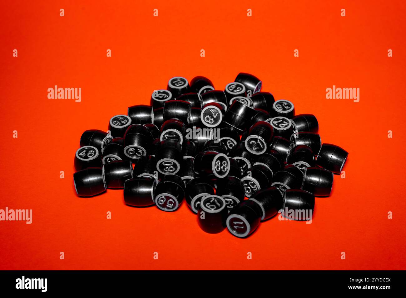 Eine Sammlung von schwarzen Bingobällen ist über eine leuchtend orange Oberfläche verstreut. Jeder Ball ist nummeriert, wodurch eine ansprechende visuelle Darstellung entsteht, die Sie zeigen können Stockfoto