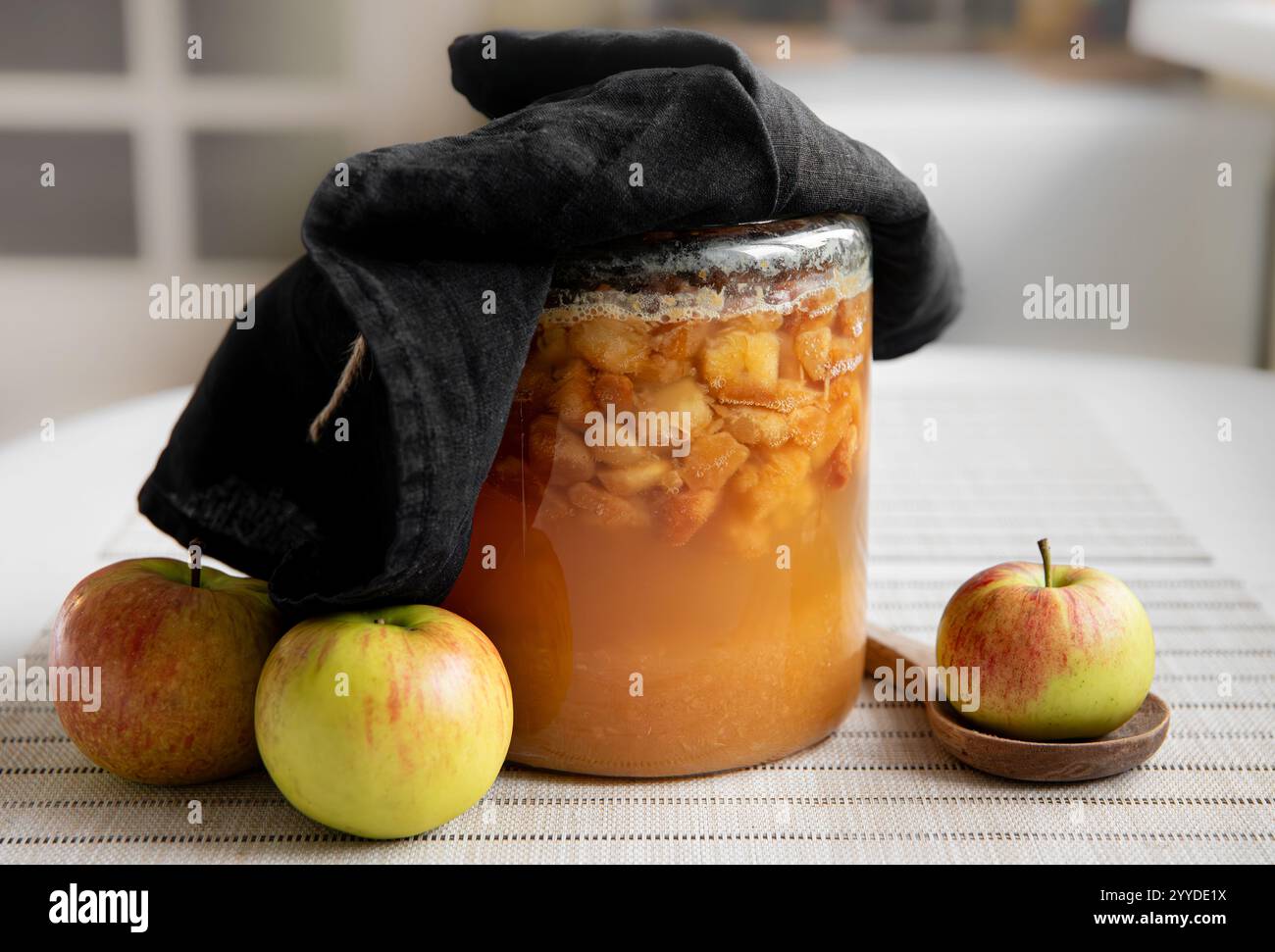 Machen Sie Ihren eigenen Apfelessig zu Hause, fermentieren Sie geschnittene Äpfel in einem Glasgefäß, der mit einem dunklen Leinentuch bedeckt ist. In Bearbeitung. Stockfoto