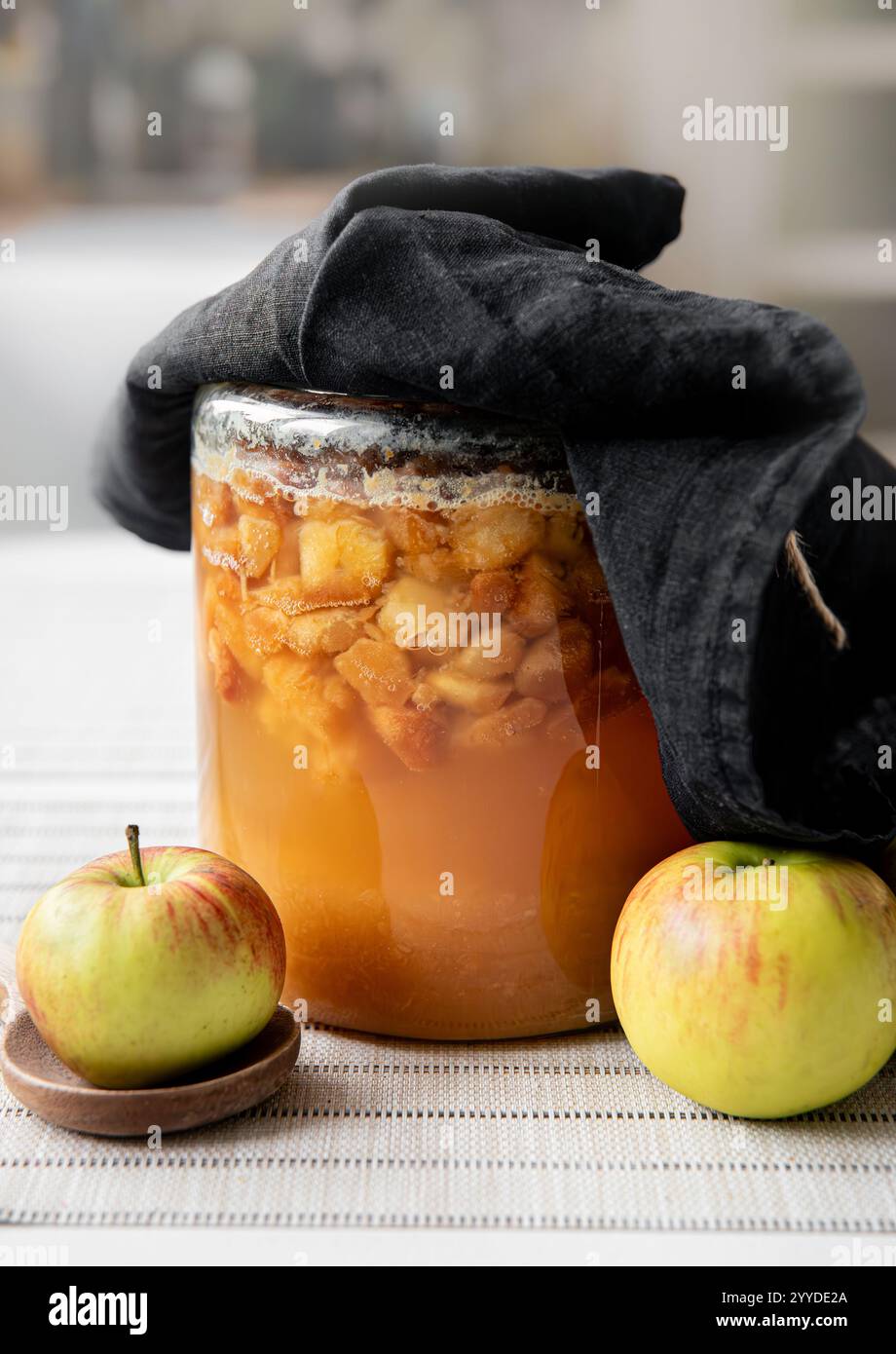 Machen Sie Ihren eigenen Apfelessig zu Hause, fermentieren Sie geschnittene Äpfel in einem Glasgefäß, der mit einem dunklen Leinentuch bedeckt ist. In Bearbeitung. Stockfoto