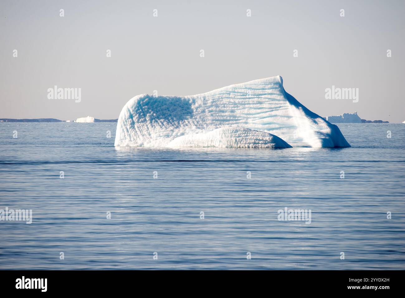 Dieses atemberaubende Bild fängt die Pracht der Eisberge in Grönland ein, die im Tageslicht unter einem leuchtend blauen Himmel getaucht sind. Das Sonnenlicht beleuchtet das Eis Stockfoto