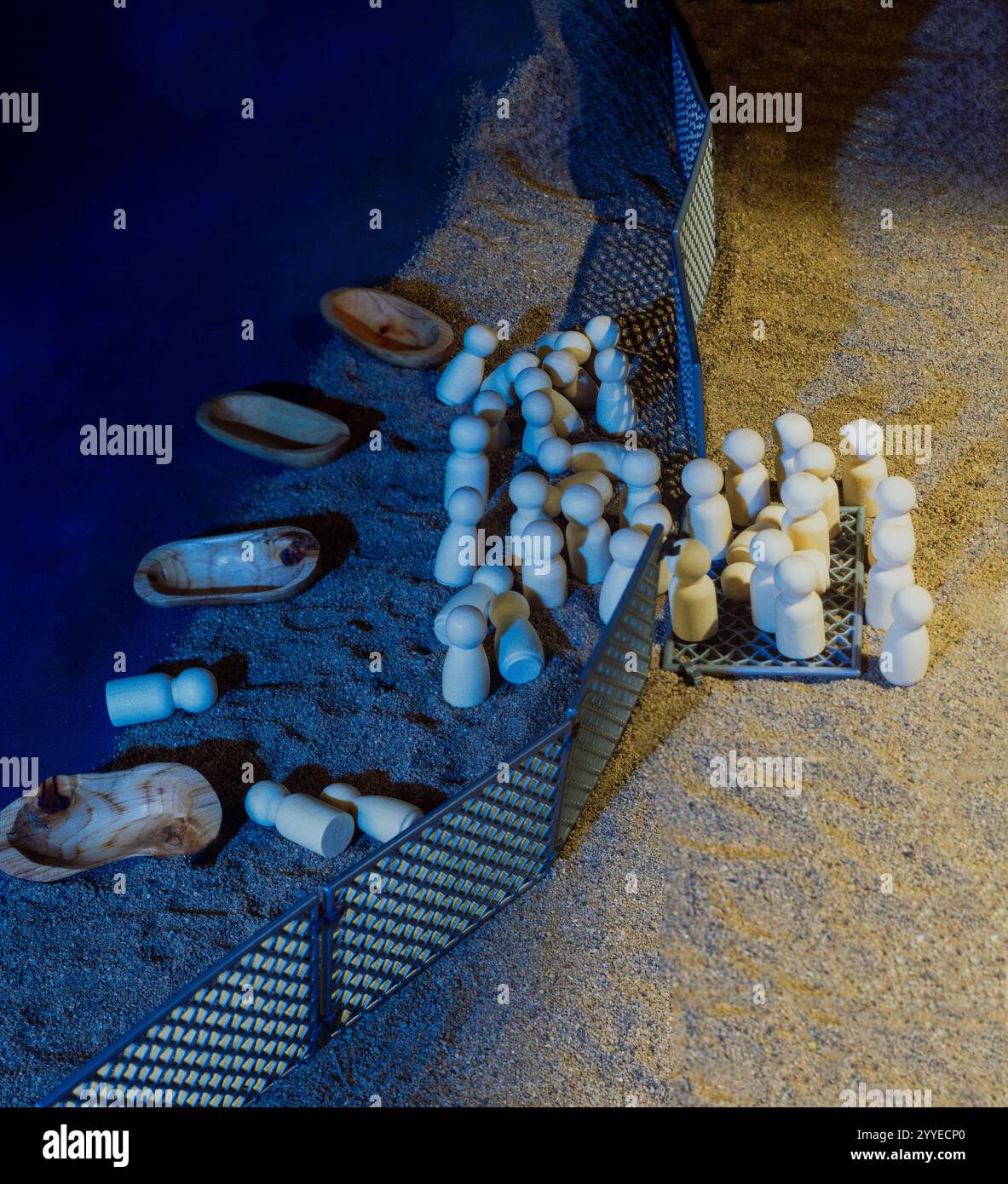 Holzpuppen und Boote in der Nähe eines Zauns in einer sandigen Umgebung, von oben erfasst, symbolisieren Migrationsherausforderungen. Stockfoto