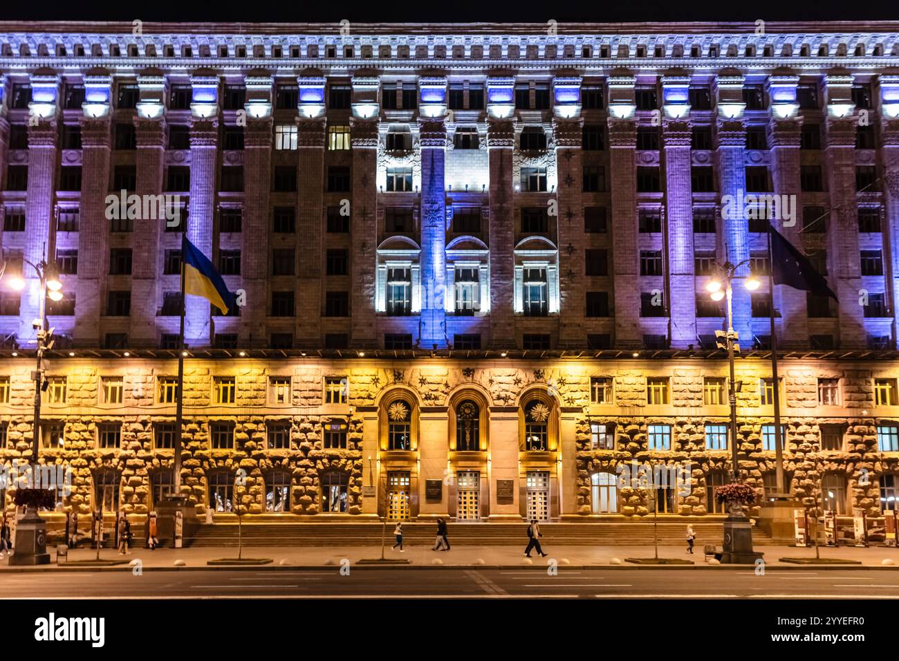 Ein großes Gebäude mit einer gelb-blauen Fassade. Das Gebäude ist nachts beleuchtet Stockfoto