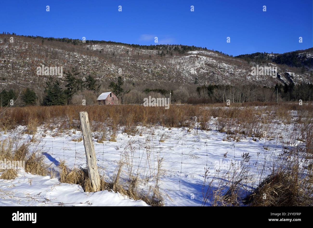 Verwitterte Scheune am Fuße eines Hügels mit einem schneebedeckten Feld und Zaunpfosten im Vordergrund Stockfoto