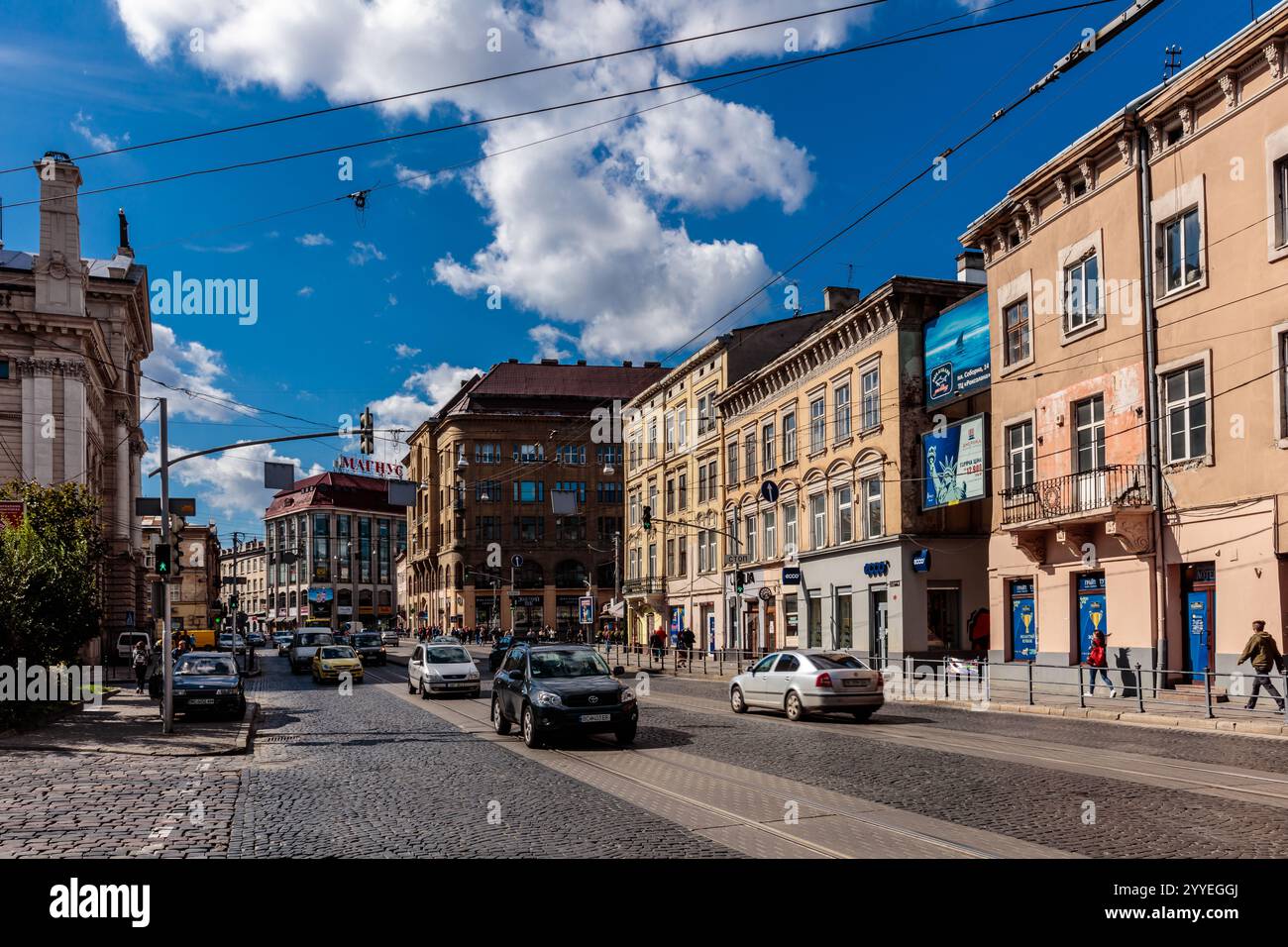 Eine geschäftige Stadtstraße mit Autos und Fußgängern. Der Himmel ist blau und es gibt Wolken. Die Gebäude sind hoch und es gibt viele Leute, die herumlaufen Stockfoto