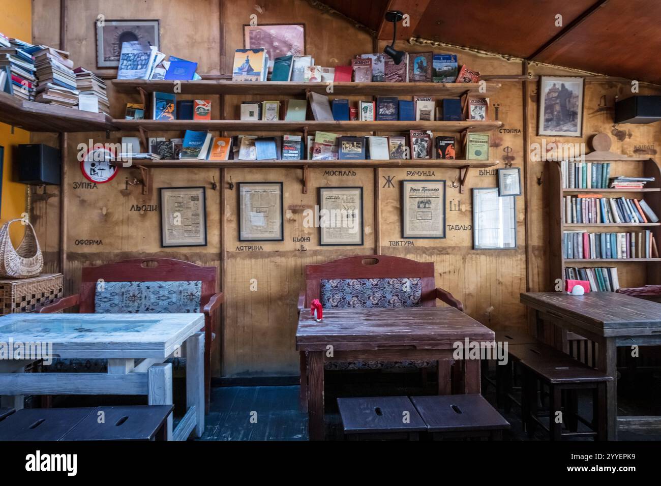 Ein kleines Café mit Holztischen und -Stühlen und einer Wand voller Bücher. Die Atmosphäre ist gemütlich und einladend Stockfoto