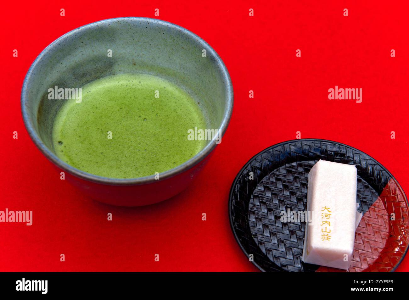 Japanischer aufschäumender Bittertee-Zeremonie Tee namens „Matcha“ wird in einer Porzellanschale serviert, begleitet von einem traditionellen süßen Snack namens „okashi“, Japan. Stockfoto