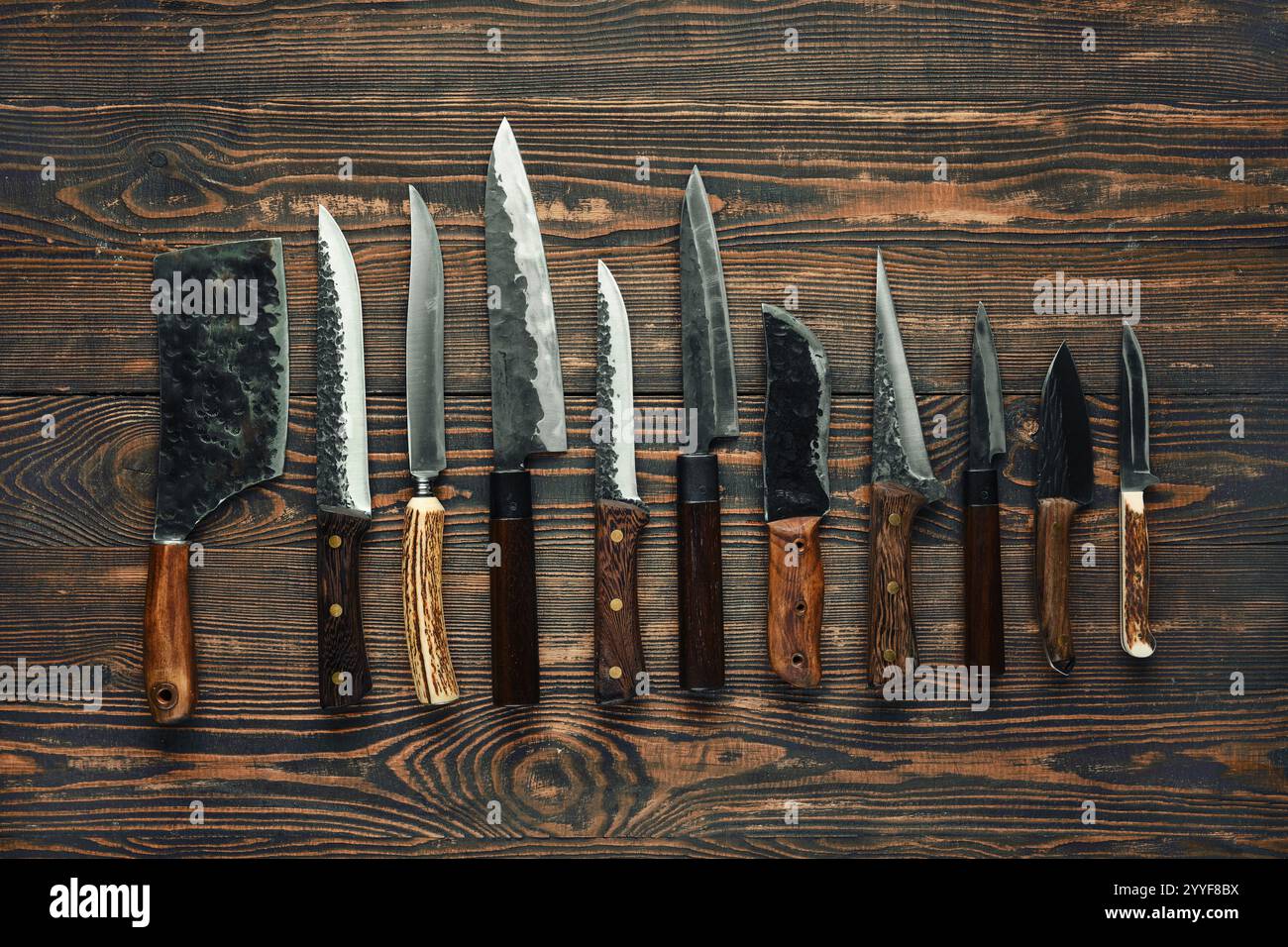 Verschiedene Küchenmesser sind ordentlich auf einem rustikalen Holztisch angeordnet und zeigen verschiedene Formen und Größen, einschließlich Trennmesser, Universalmesser und che Stockfoto
