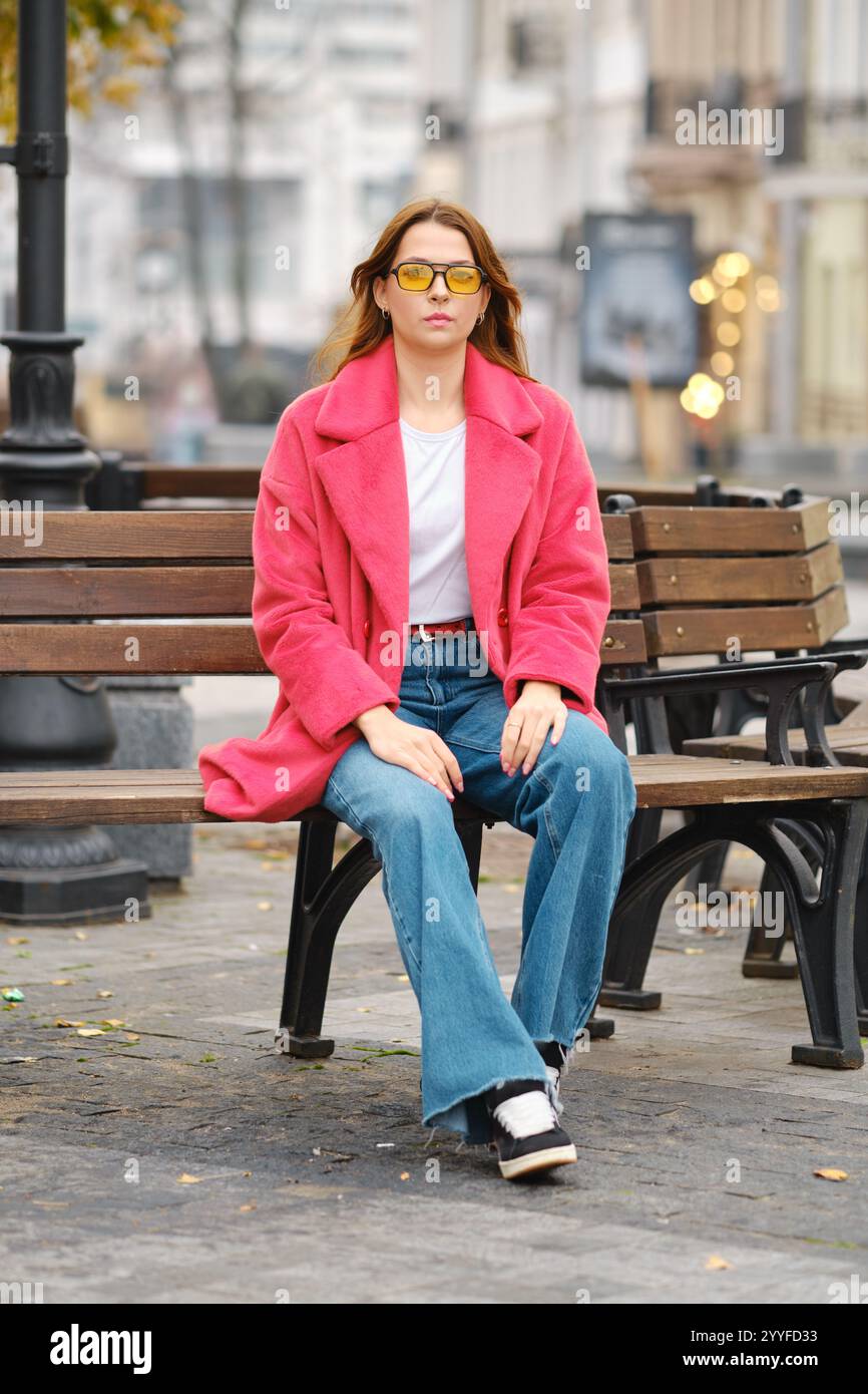 Eine junge Frau sitzt lässig auf einer Bank und genießt die urbane Atmosphäre um sie herum, während sie einen Schwarm zeigt Stockfoto