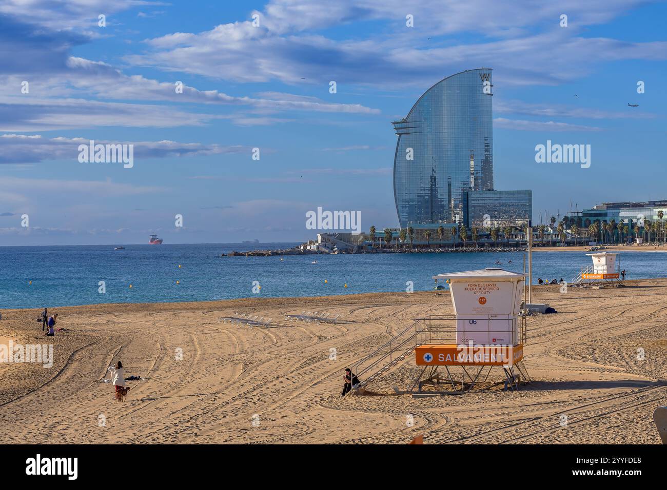 Sonniger Strand in Barcelona mit dem berühmten W Hotel, einem Rettungsschirm-Turm und einem ruhigen Mittelmeer unter einem leuchtend blauen Himmel Stockfoto