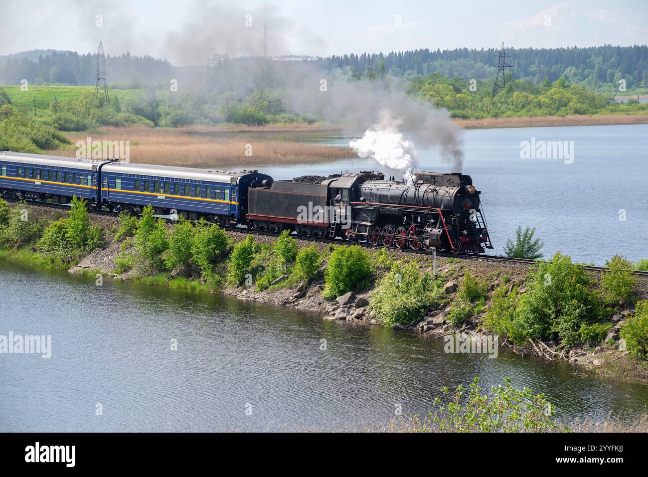 KARELIEN, RUSSLAND - 11. JUNI 2022: Retro-Dampflokomotive mit Personenzug „Ruskeala Express“ auf dem Damm des Sees. Karelien, Russland Stockfoto
