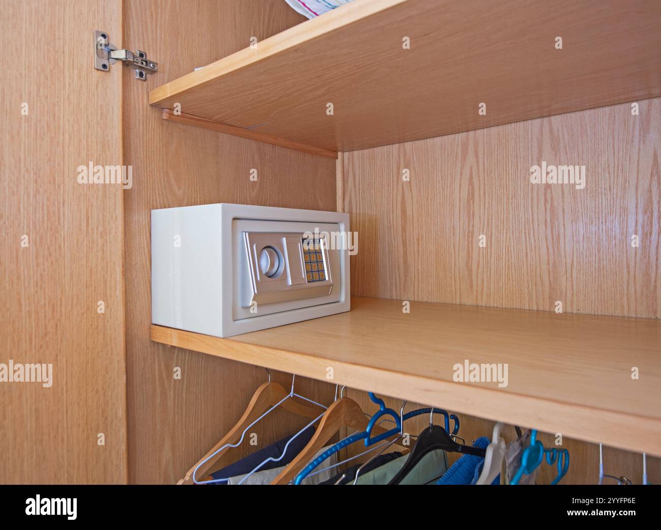 Nahaufnahme eines kleinen Safe für persönliche Sicherheit auf einem Holzregal im Kleiderschrank des Schlafzimmers mit Kleidung hängen Stockfoto