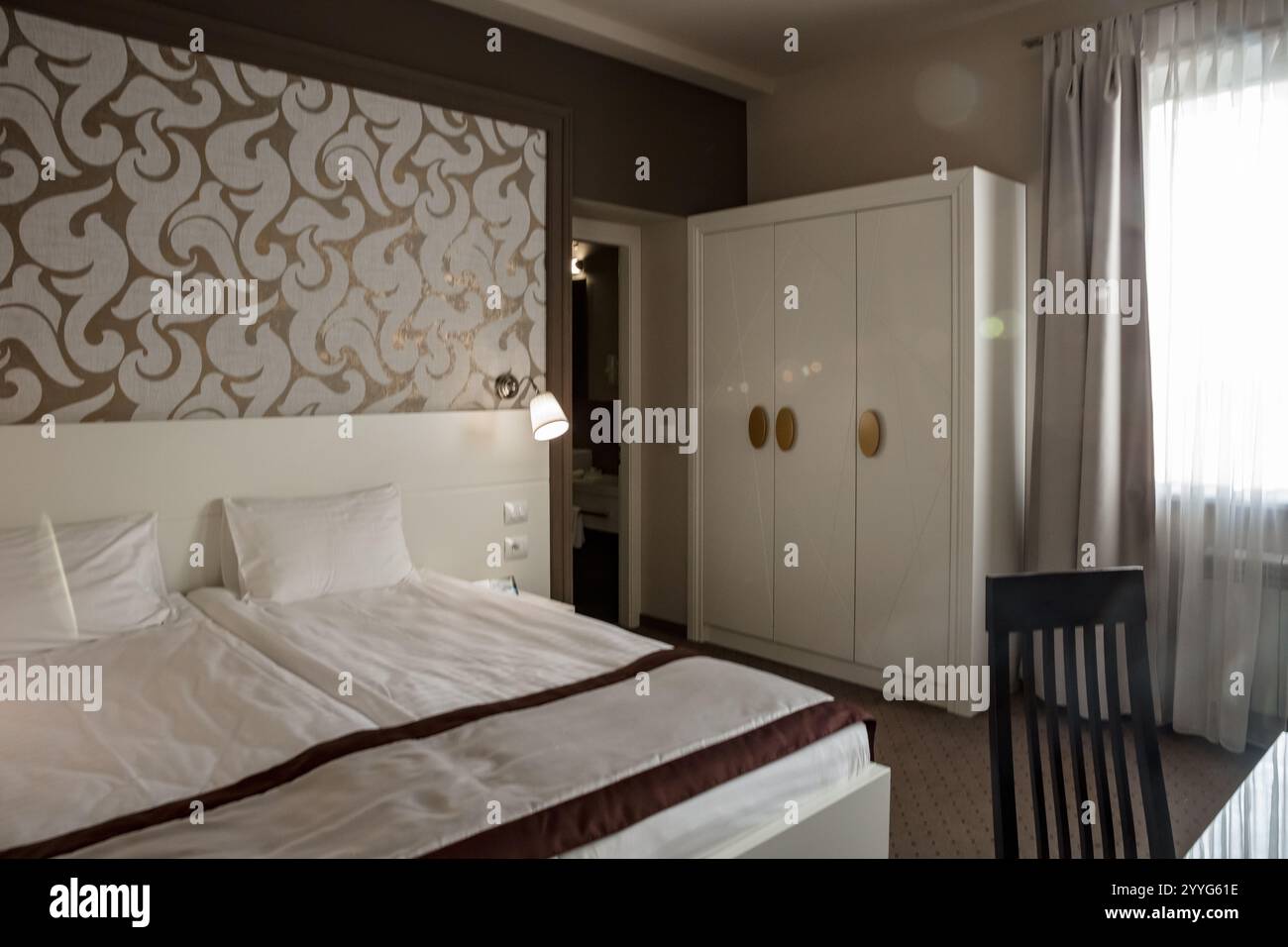 Ein Schlafzimmer mit einem weißen Bett und einer braunen Bettdecke. Das Bett ist nicht gemacht und das Zimmer ist leer Stockfoto
