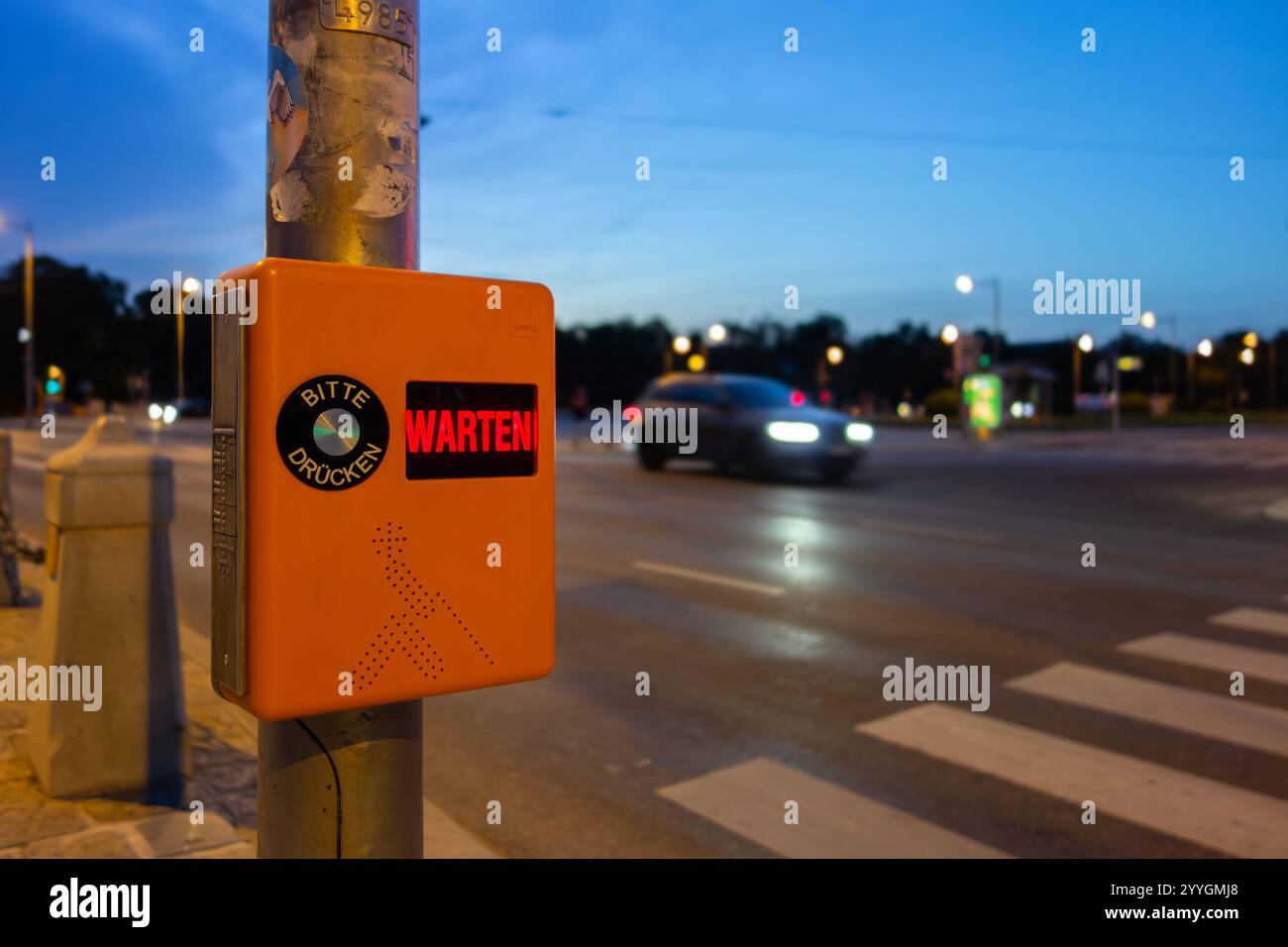 Fußgänger-Zebraüberquerung mit Text, der die Leute auffordert, zu warten und die Taste in deutscher Sprache zu drücken Stockfoto