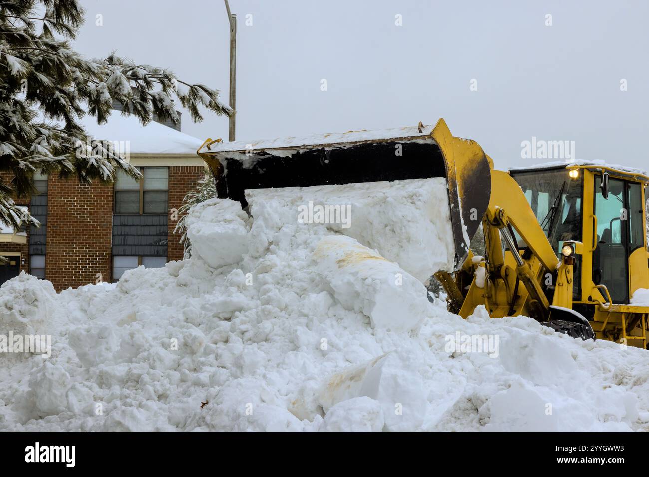 Der Schneelader räumt während des Wintersturms aktiv schwere Schneehaufen von Wohnstraßen ab. Stockfoto