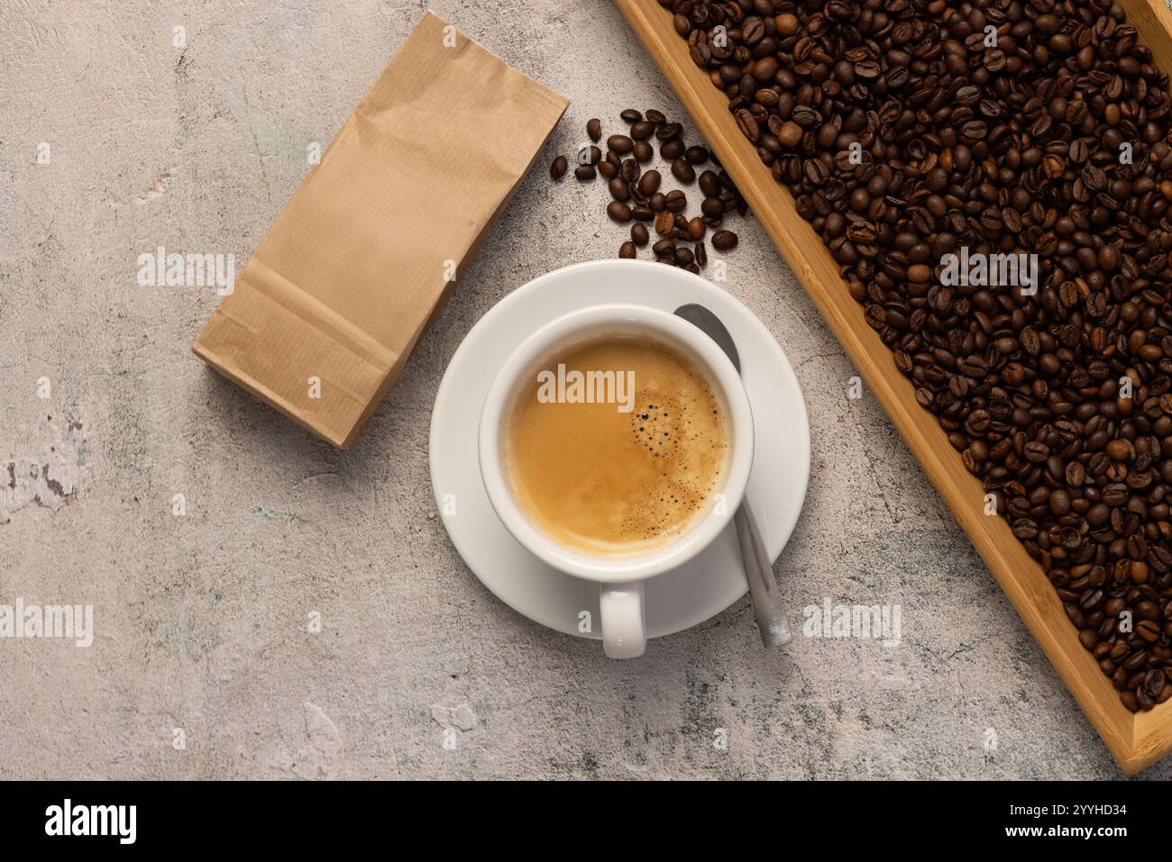 Eine Tasse heißen Kaffee mit Crema und eine braune Papiertüte Kaffeebohnen an der Seite. Stockfoto