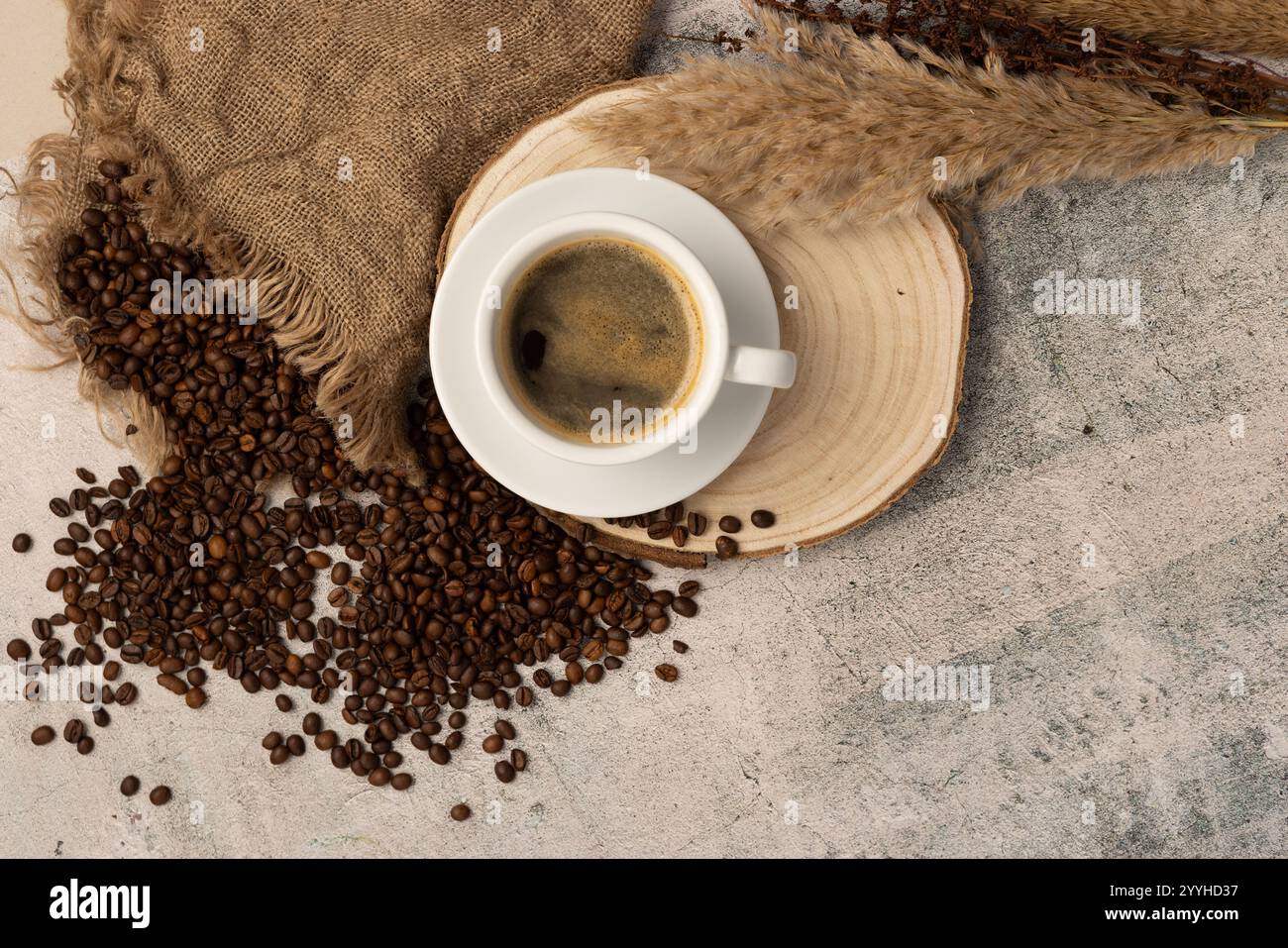 Eine Tasse Americano-Kaffee mit einer reichhaltigen Crema-Schicht - die Tasse und Untertasse wird auf eine Scheibe aus natürlichem Baumschnitt von oben, verschütteten Bohnen und Flora gelegt Stockfoto