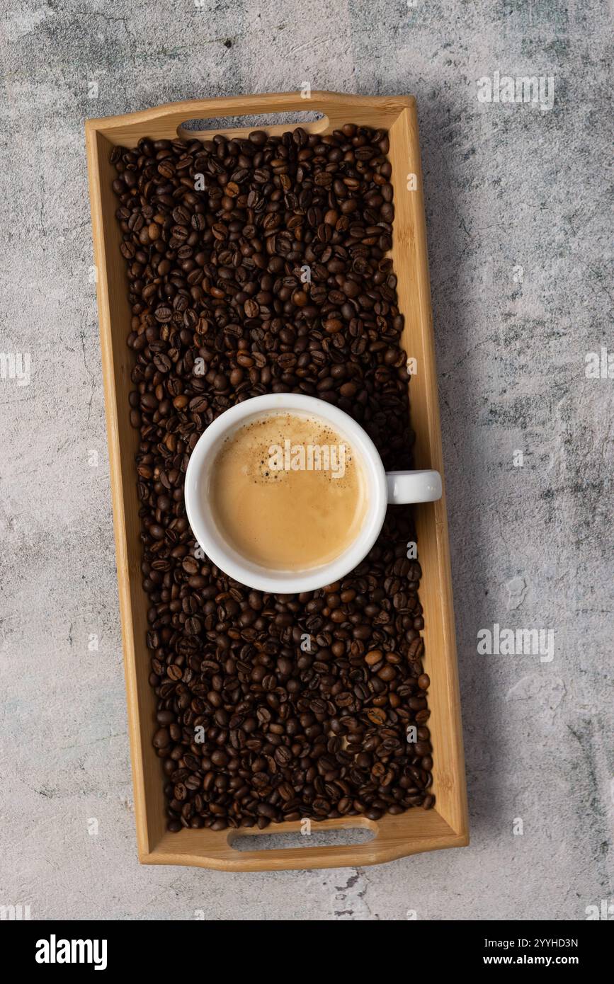 Ein Blick von oben auf einen schwarzen Americano-Kaffee mit einer reichhaltigen Crema-Schicht. Die Tasse wird auf ein Tablett mit rohen Kaffeebohnen gestellt. Stockfoto