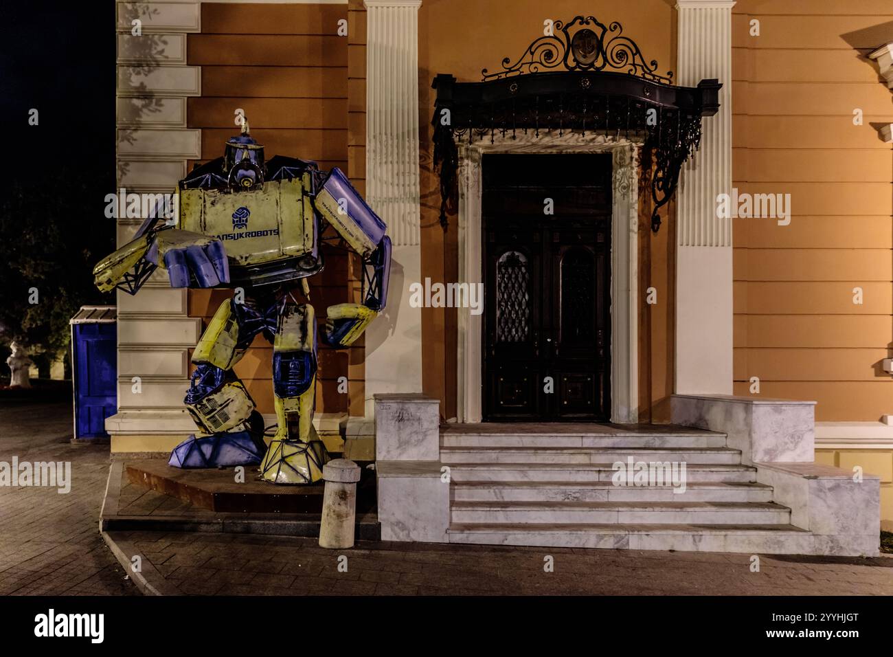 Ein Roboter steht vor einem Gebäude mit einer blauen Box an der Wand. Der Roboter trägt einen blau-gelben Anzug Stockfoto