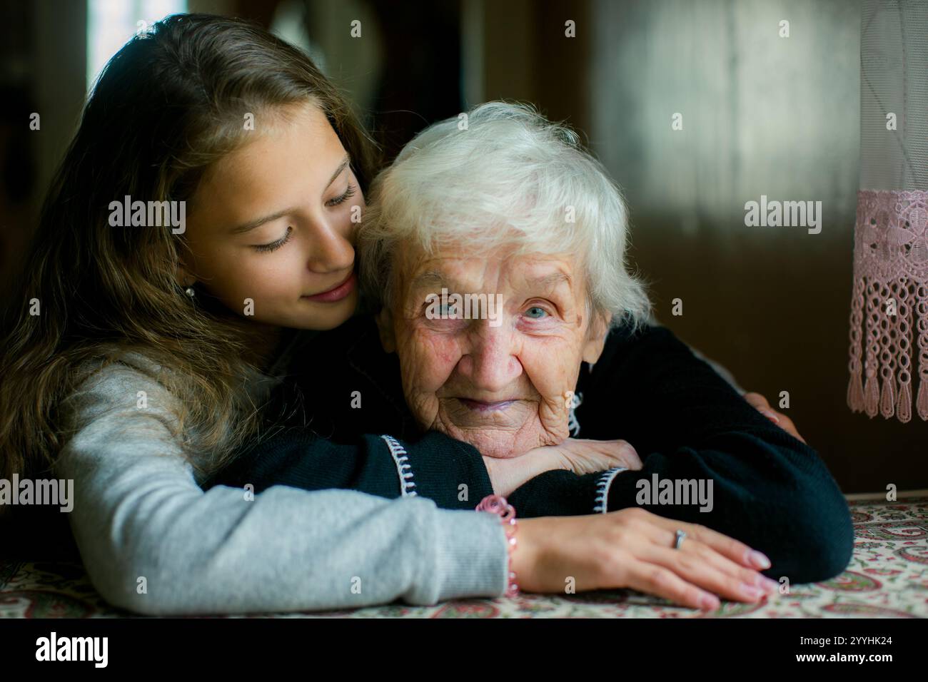 Ein Porträt einer Großmutter mit einem sanften Lächeln, während ihre Teenager-Enkelin sie liebevoll umarmt und eine innige Verbindung aufnimmt. Stockfoto