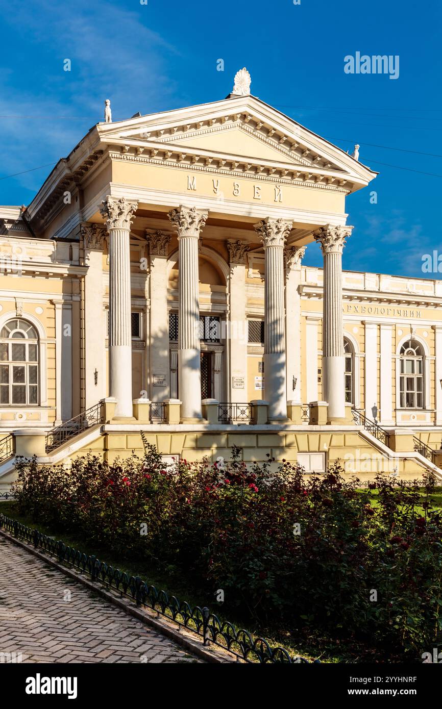 Ein großes Gebäude mit einer weißen Fassade und einem roten Dach. Das Gebäude hat einen großen Torbogen und einen Balkon. Das Gebäude ist von einem üppig grünen Garten umgeben Stockfoto