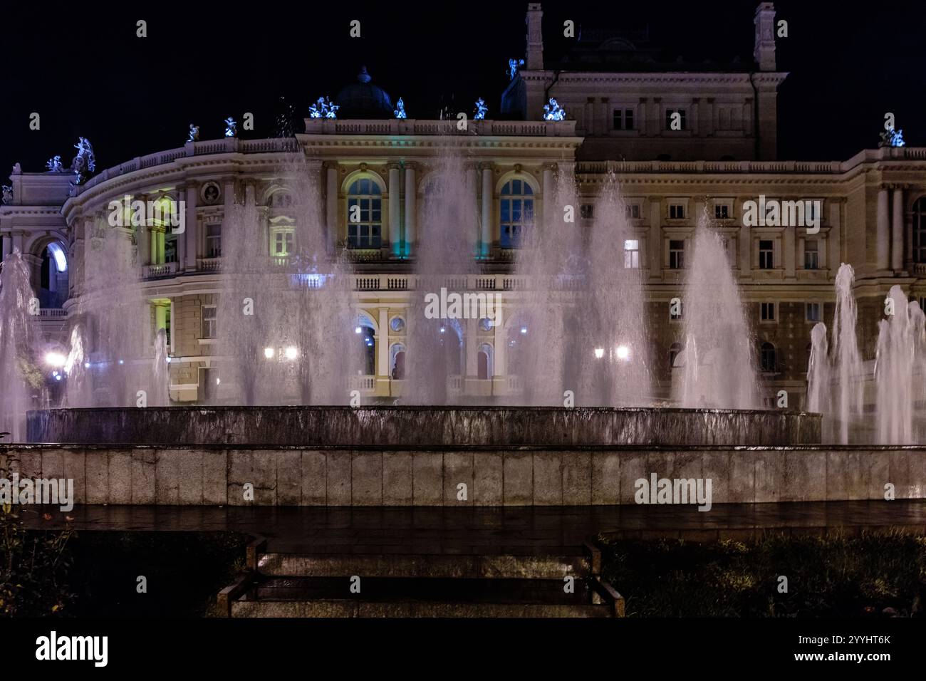 Ein großer Brunnen mit einem Gebäude im Hintergrund. Der Brunnen ist nachts beleuchtet Stockfoto