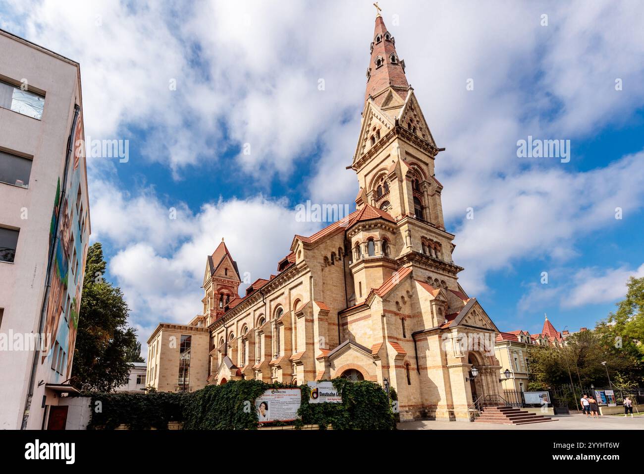Eine große Kirche mit einem Turm und einem Uhrenturm. Das Gebäude ist von Bäumen und Büschen umgeben Stockfoto