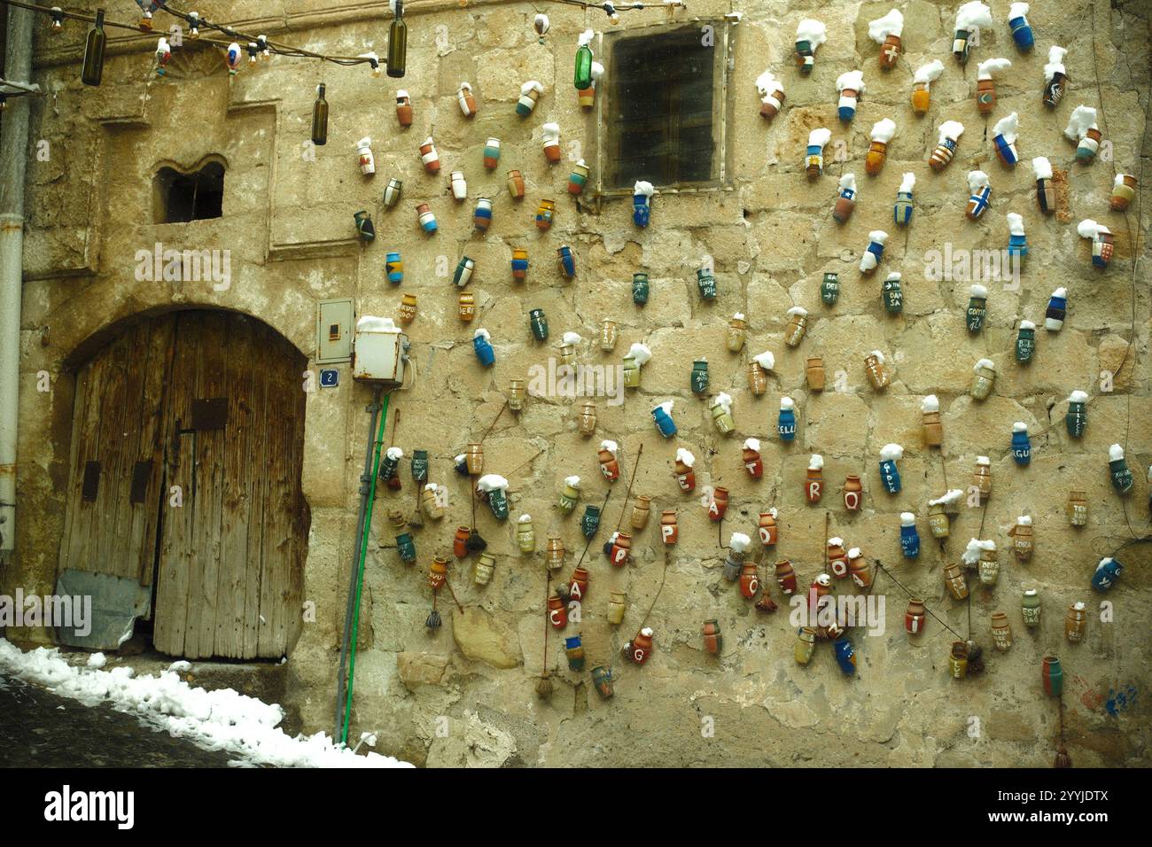 Göreme, Kappadokien, Türkiye - 25. November 2024: Farbenfrohe künstlerische und einzigartige Töpferwaren hängen an einem alten Steinfassadengebäude als dekorative Mauer Stockfoto