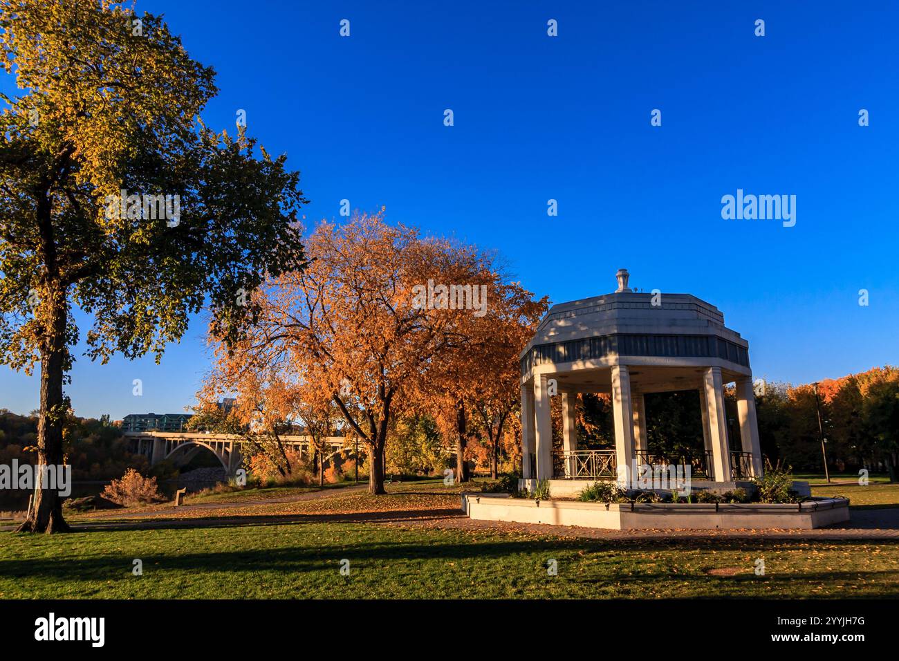Ein Park mit Pavillon und Bäumen im Hintergrund. Der Pavillon ist leer. Der Himmel ist blau und die Sonne untergeht Stockfoto