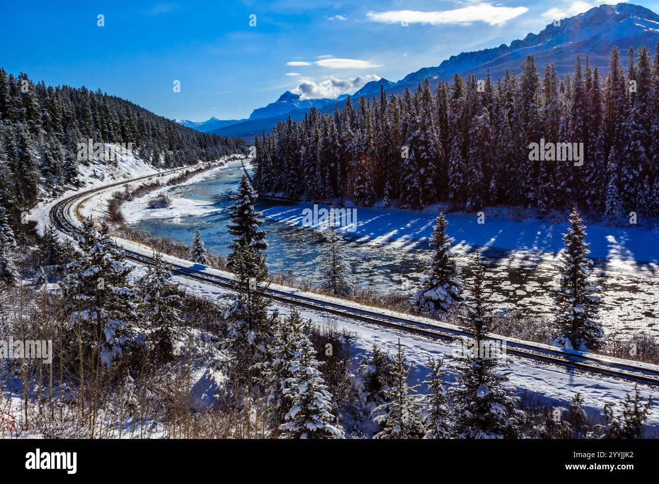 Eine verschneite Bergkette befindet sich im Hintergrund einer Bahnstrecke. Der Zug fährt die Gleise entlang, und der Schnee bedeckt die Bäume. Die Szene ist Stockfoto