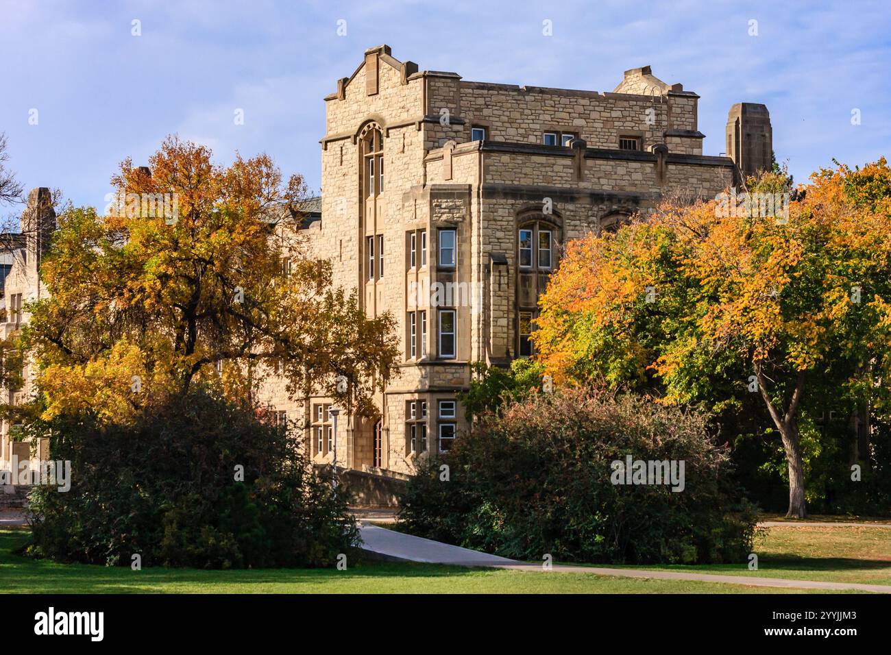 Ein großes Gebäude mit vielen Fenstern und einer Backsteinfassade. Das Gebäude ist von Bäumen umgeben, deren Blätter sich ändern. Die Szene ist friedlich Stockfoto