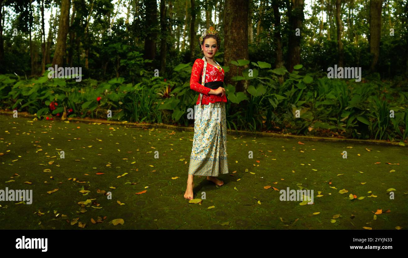 Ein traditioneller Tänzer namens Ronggeng steht mit einem Ausdruck voller Schönheit und Schönheit in einem magischen Wald am Nachmittag Stockfoto