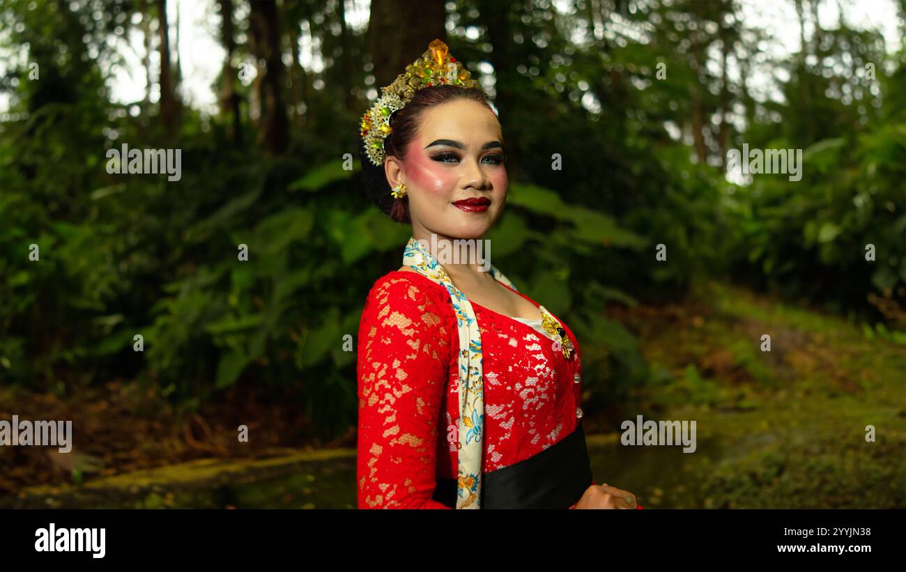 Ein traditioneller Tänzer namens Ronggeng steht mit einem Ausdruck voller Schönheit und Schönheit in einem magischen Wald am Nachmittag Stockfoto