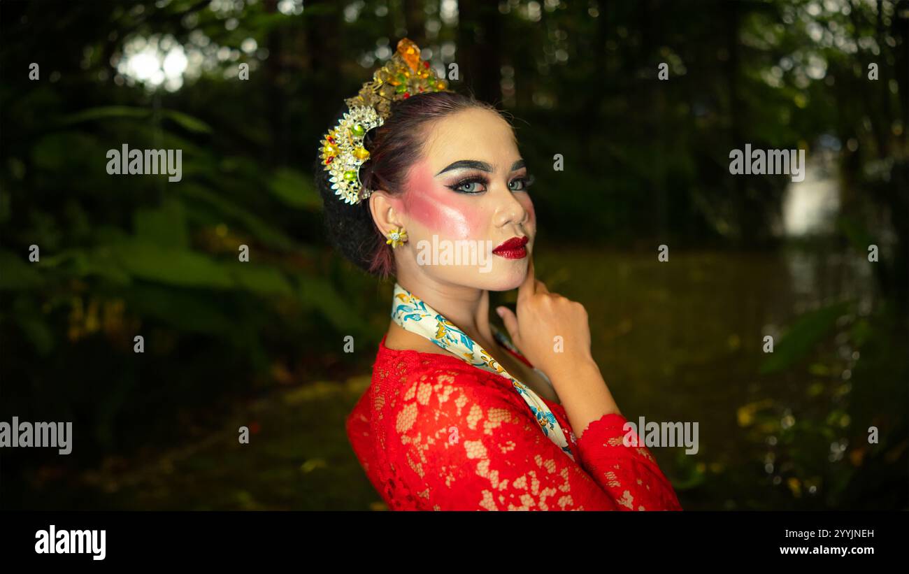 Ein traditioneller Tänzer namens Ronggeng steht mit einem Ausdruck voller Schönheit und Schönheit in einem magischen Wald am Nachmittag Stockfoto