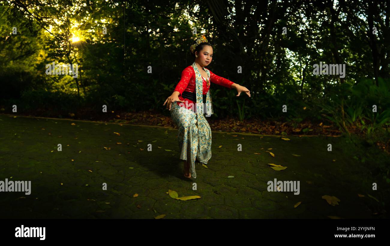Eine traditionelle indonesische Tänzerin trägt ein rotes Kostüm, das mit Pailletten und Stickerei verziert ist, sieht luxuriös aus, wenn die Tänzerin im Wald auftritt Stockfoto