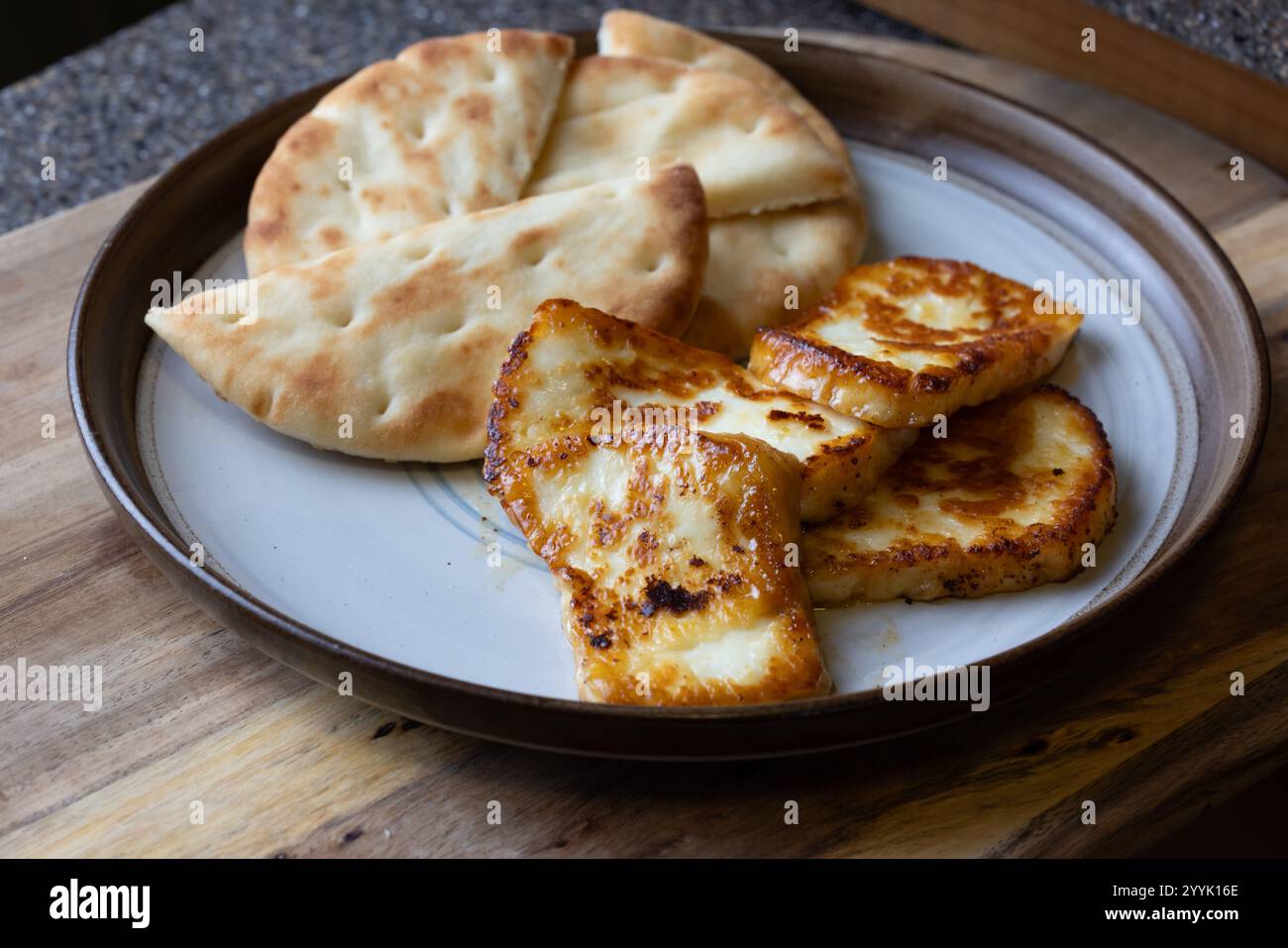 Ein Teller mit gebratenem halloumi-Käse mit einer Seite Pita-Brot. Das Essen ist goldbraun und sieht köstlich aus. Stockfoto